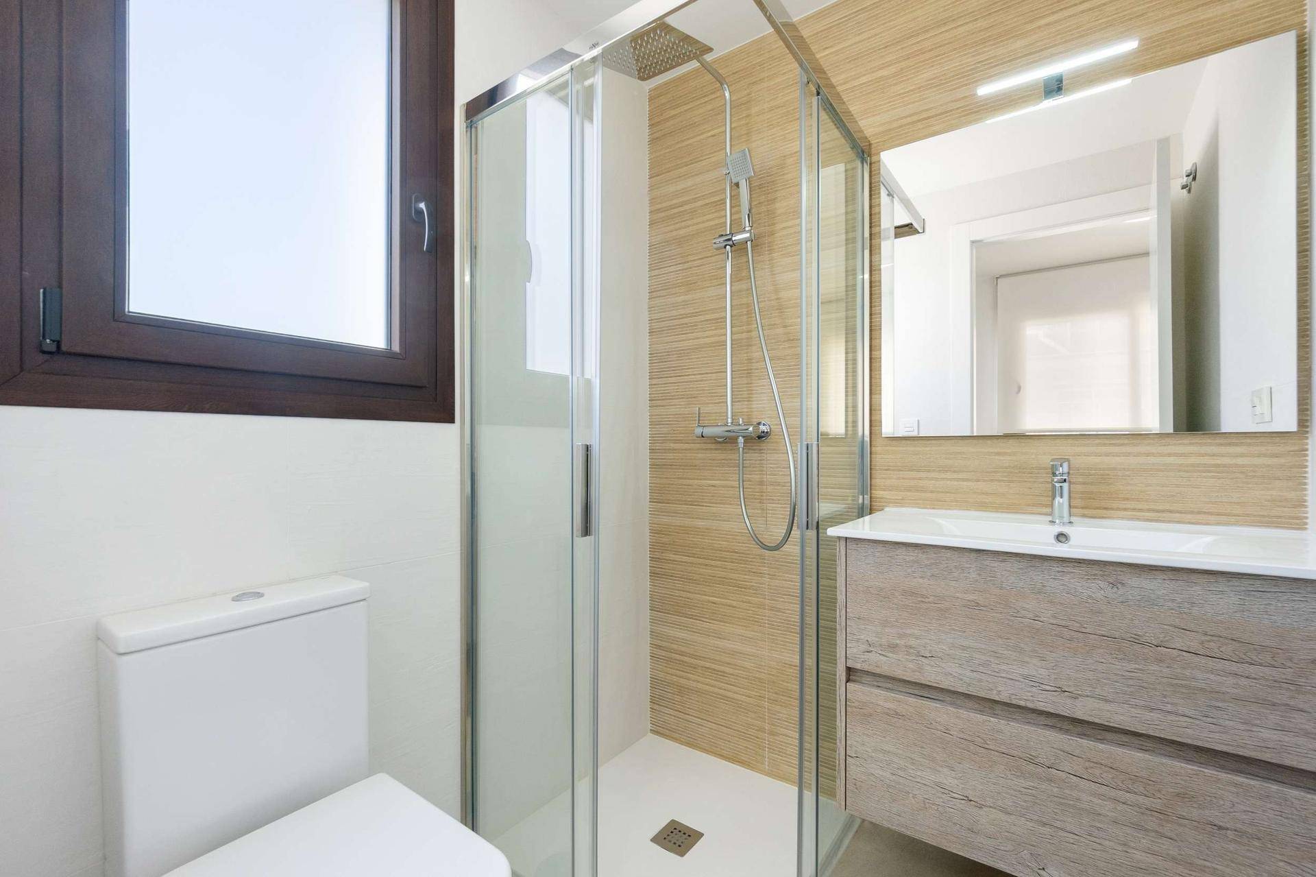 Modernes Badezimmer mit Duschkabine, WC, Waschtisch und Fenster für Tageslicht.