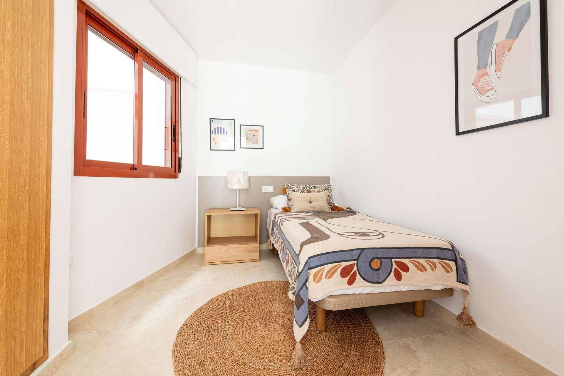 Helles Schlafzimmer mit Einzelbett, Holzboden und einem Fenster, das viel Tageslicht hereinlässt.