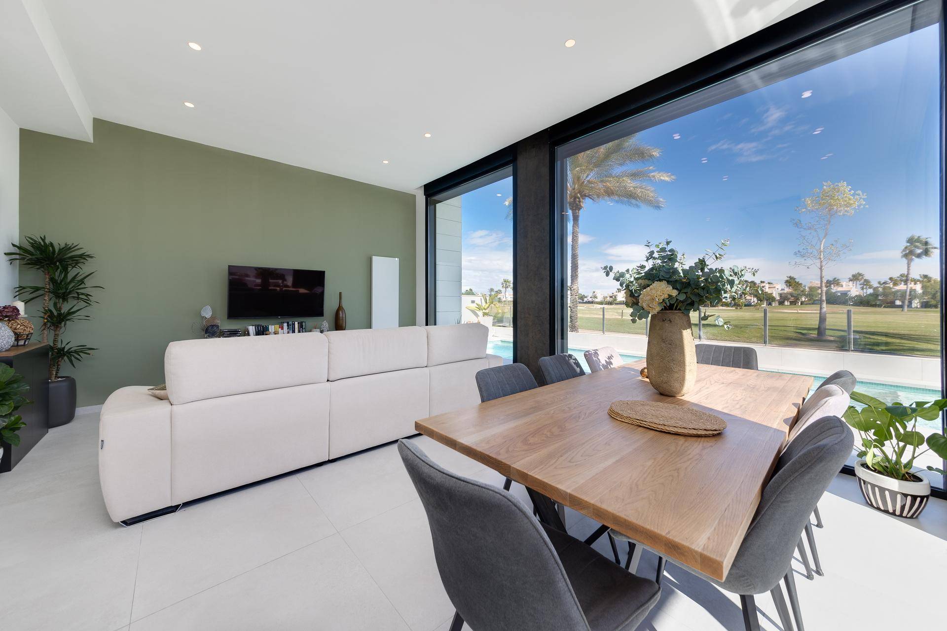 Heller Wohn- und Essbereich mit beigem Sofa und großen Fenstern mit Poolblick.