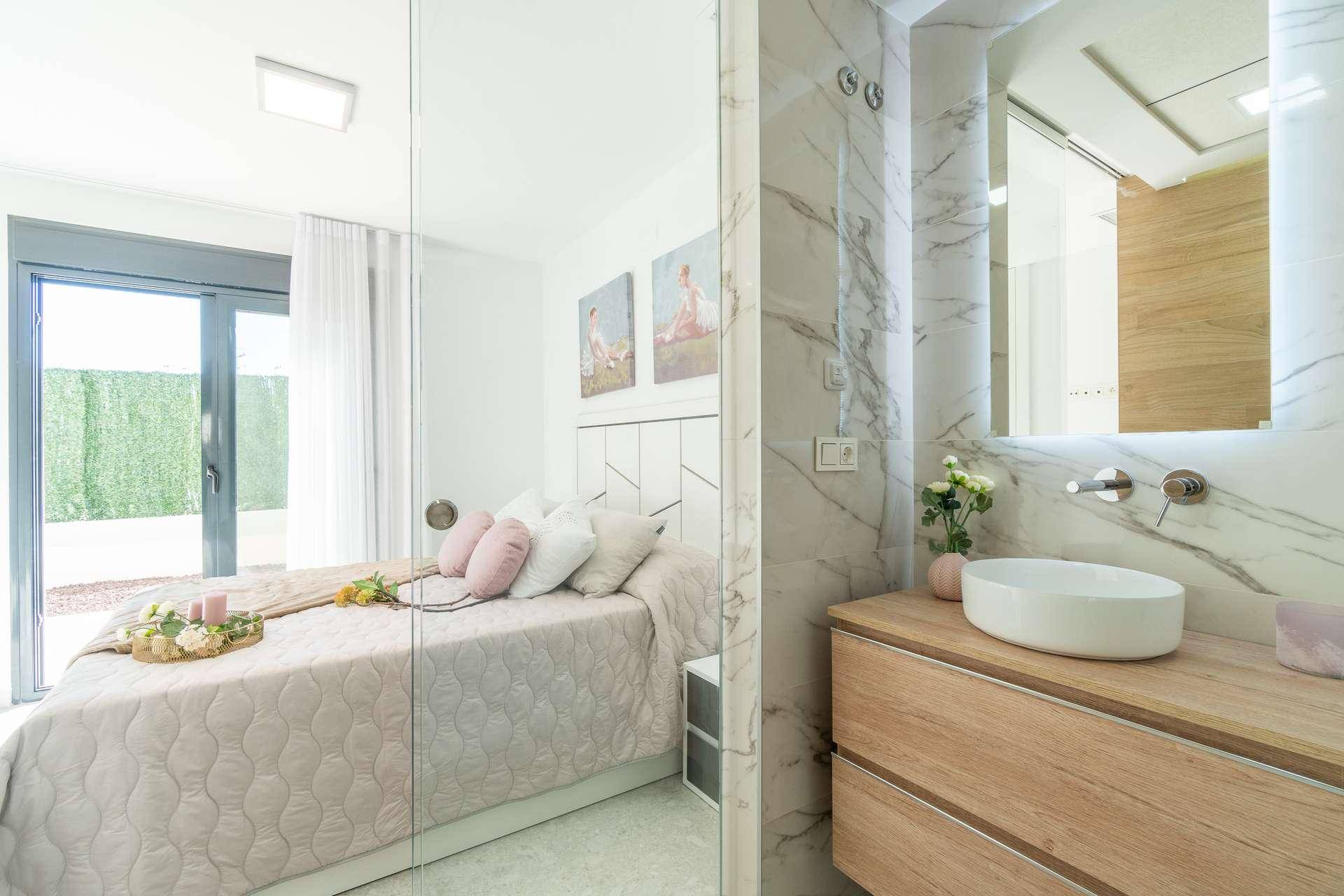 Modernes Schlafzimmer mit Zugang zu einem luxuriösen Bad mit Marmorfliesen und Waschtisch.