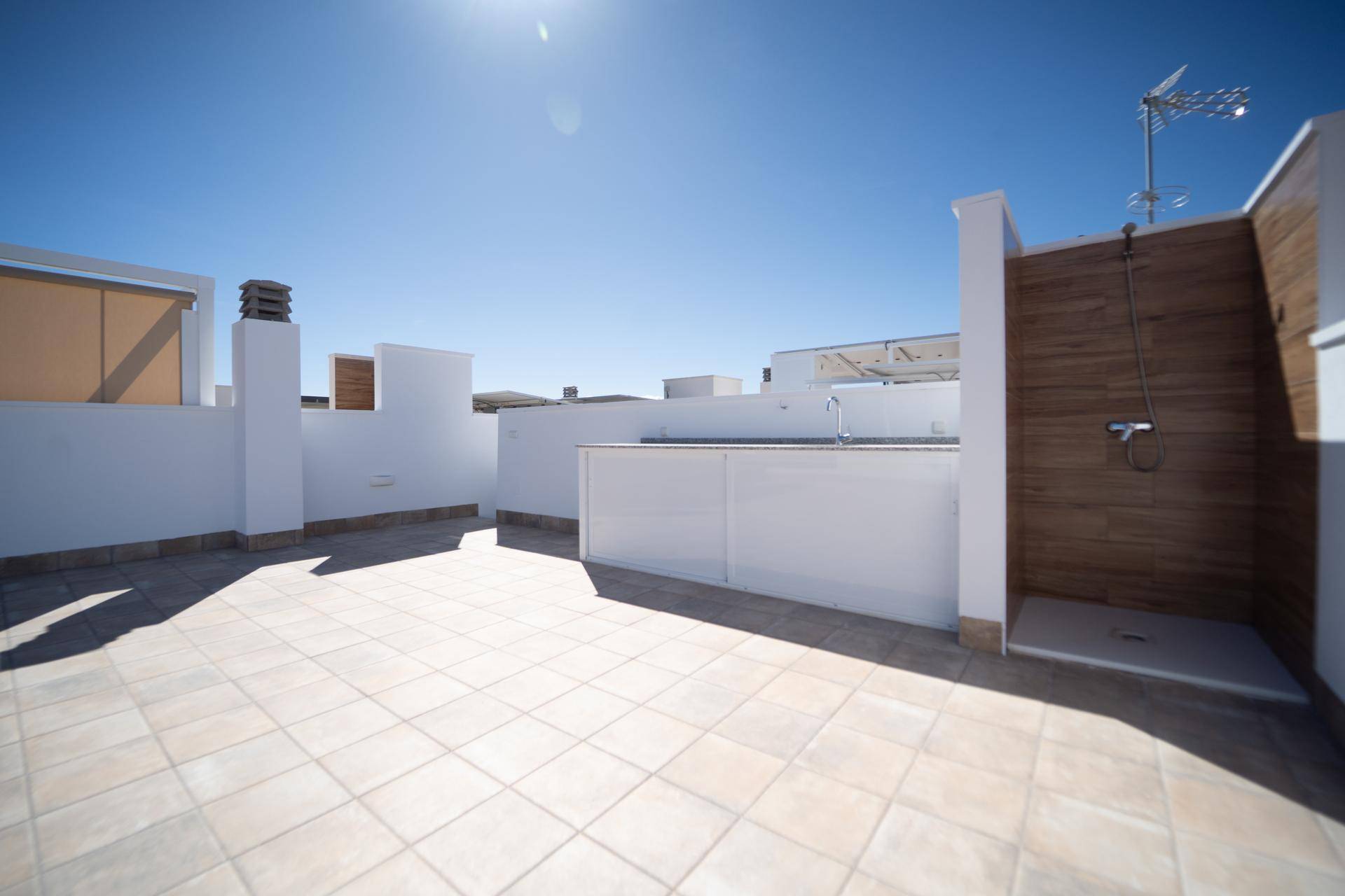 Geräumige Dachterrasse mit Außenküche, Dusche und Fliesenboden unter blauem Himmel.