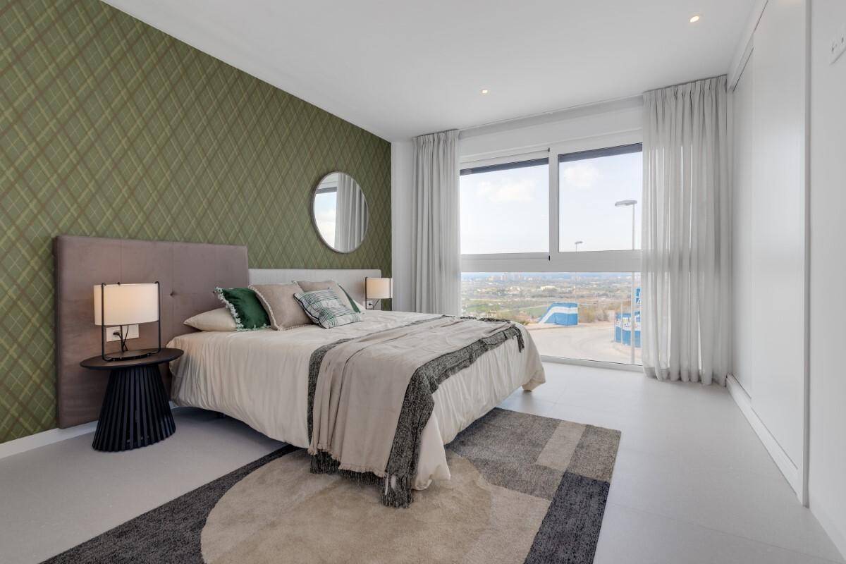 Schlafzimmer mit grüner Akzentwand, großem Fenster und Blick ins Grüne.