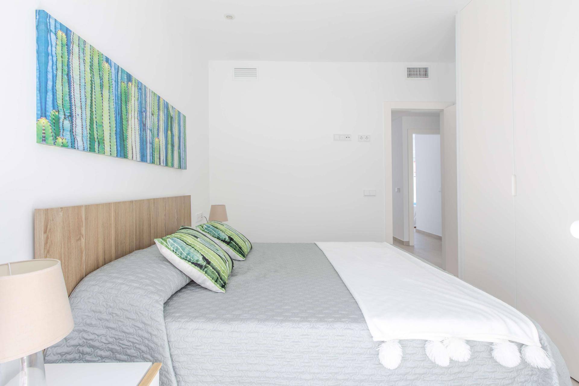 Schlafzimmer mit modernem Kunstwerk über dem Bett, weißen Wänden und Einbauschränken.