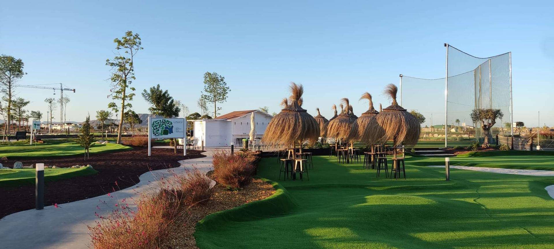 Gepflegte Minigolfanlage mit Grünflächen und schattenspendenden Strohschirmen.