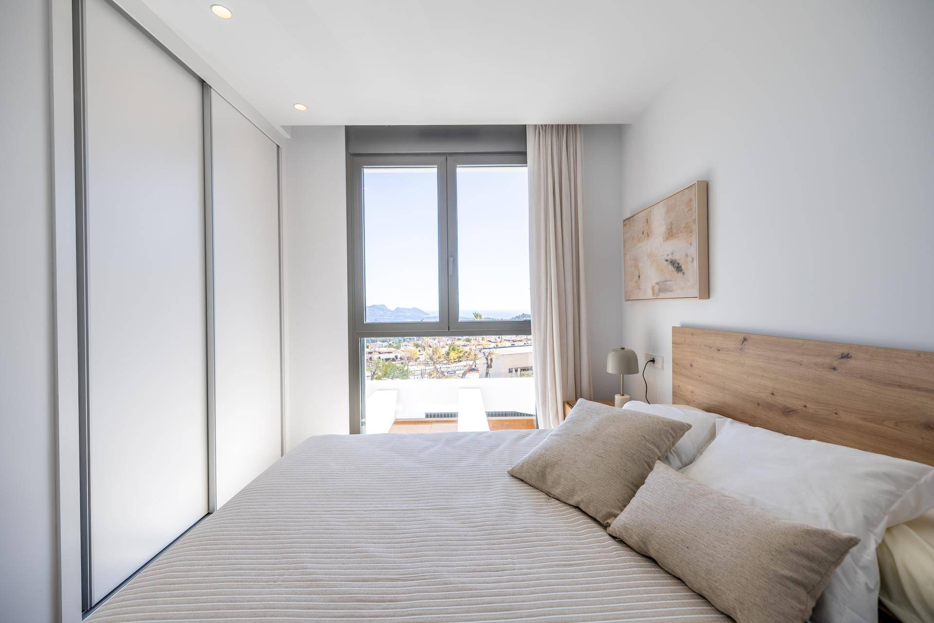 Modernes Schlafzimmer mit Einbauschrank, Holzkopfteil und weitem Ausblick auf die Umgebung.