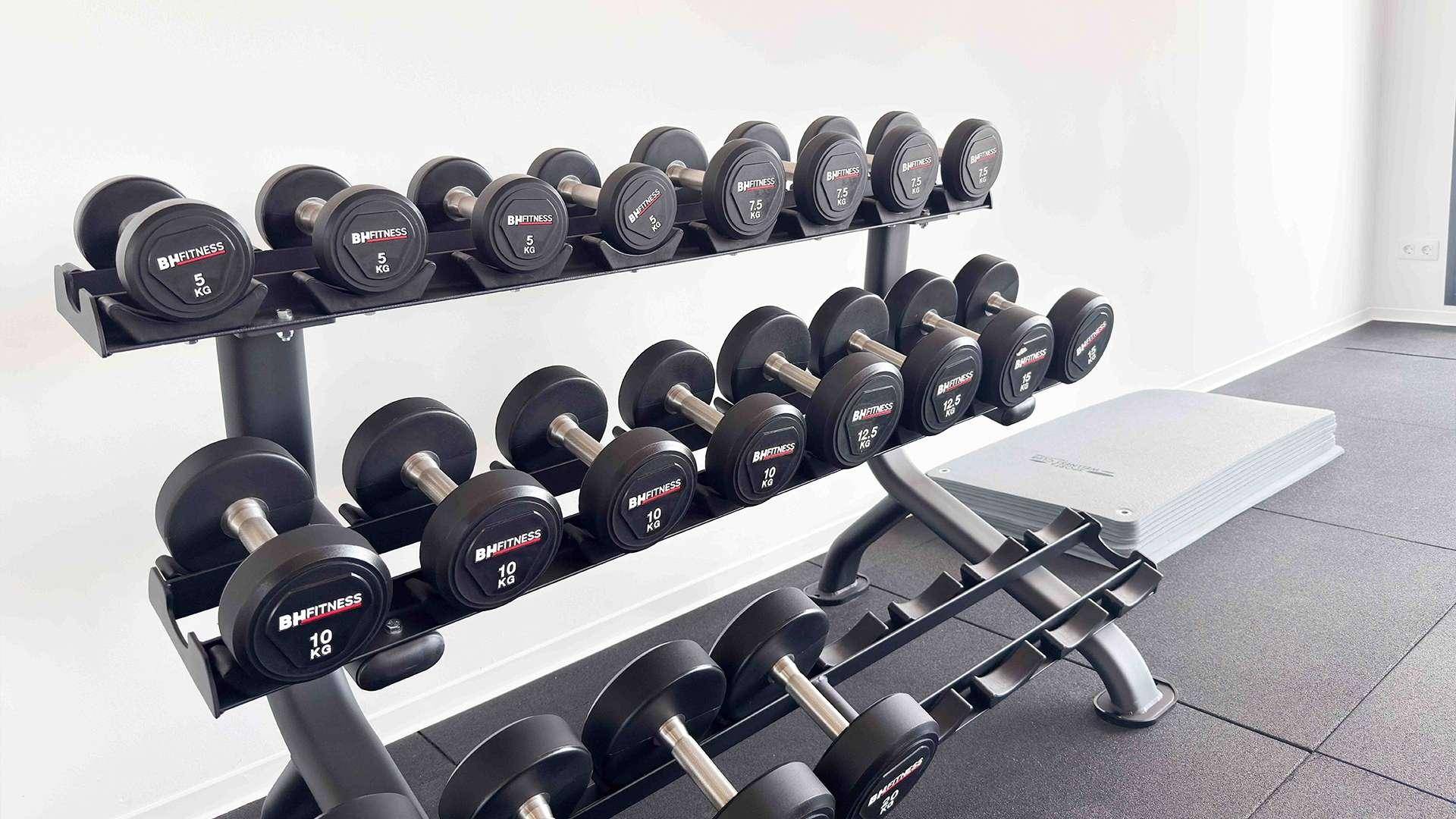Hantelregal mit verschiedenen Gewichten in einem gut ausgestatteten Fitnessraum.