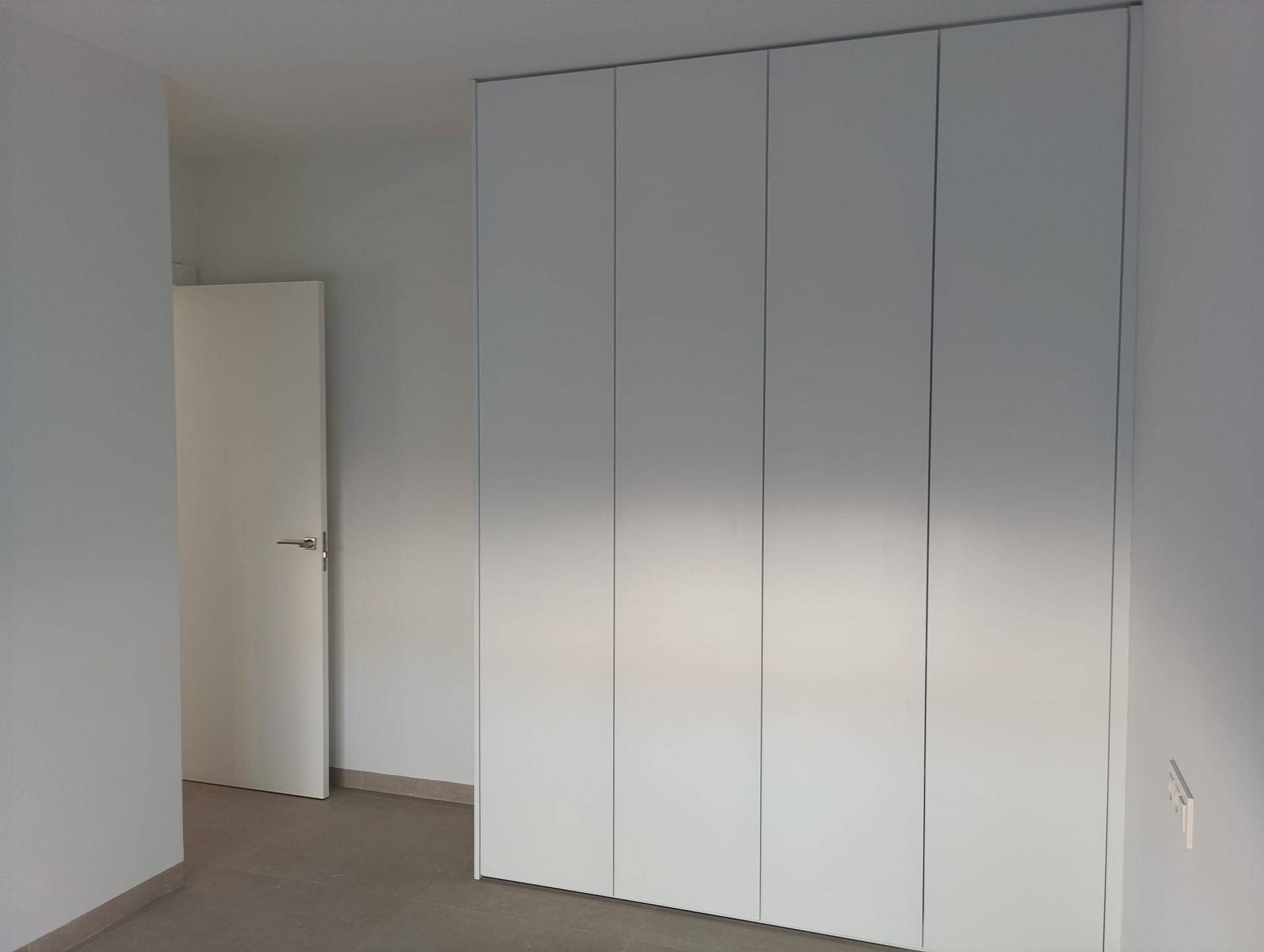Geräumiger Einbauschrank mit weißen Türen und viel Stauraum in einem hellen Zimmer.