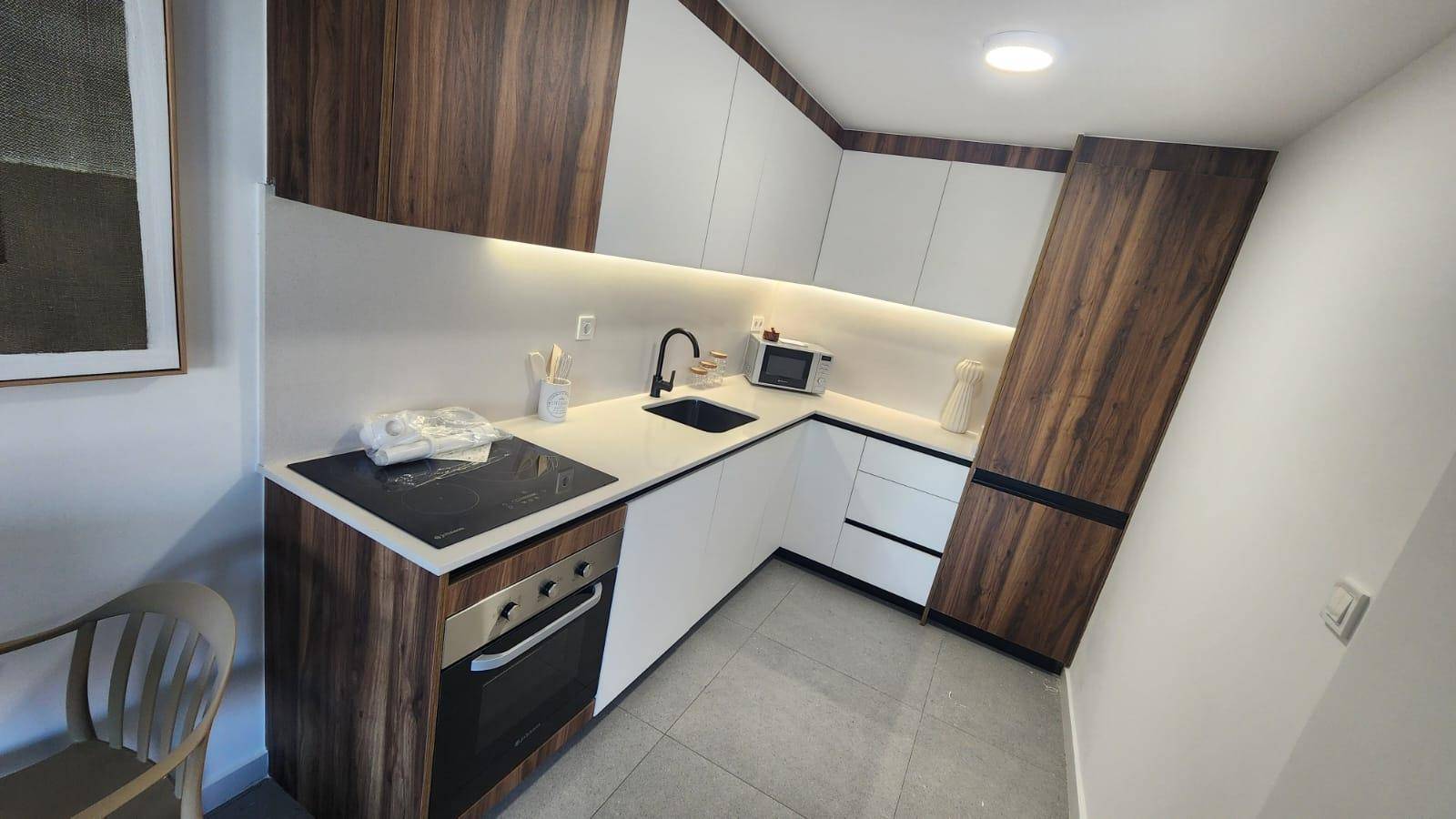 Moderne Küche mit Holz- und weißen Schränken, Induktionskochfeld und Backofen.
