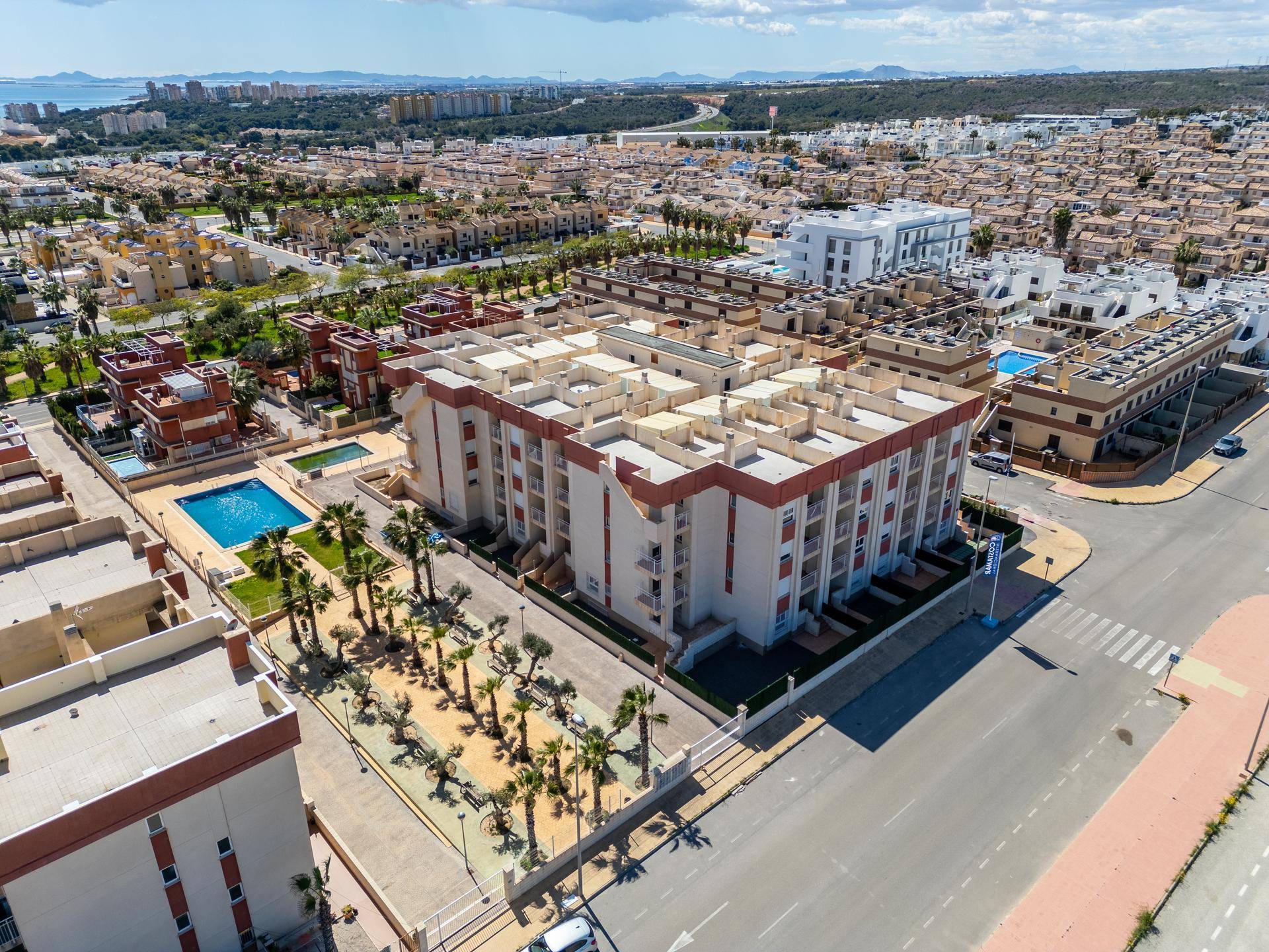 Gesamtansicht des Wohnkomplexes mit Gebäuden, Pools und der städtischen Umgebung unter blauem Himmel.