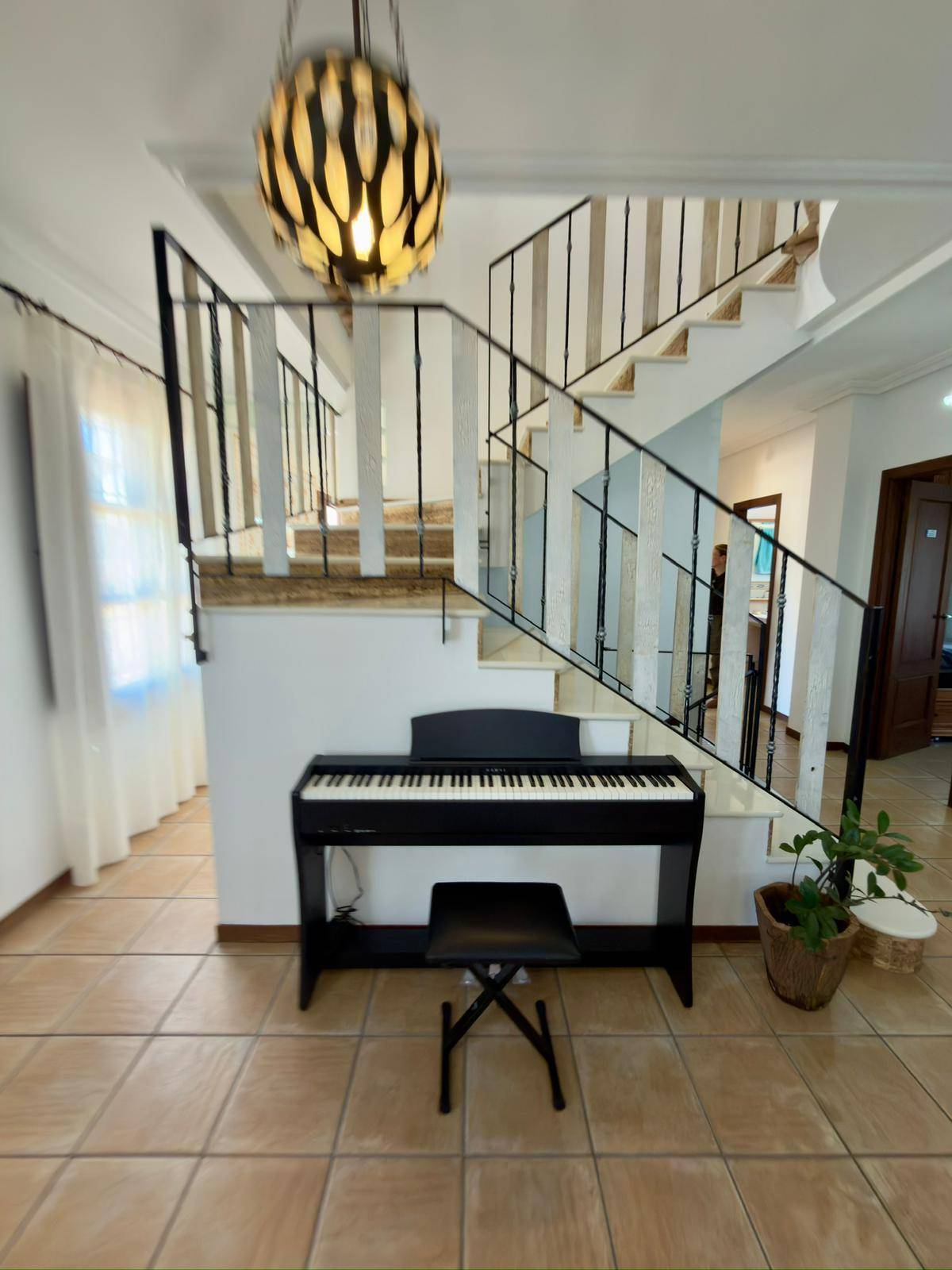 Heller Flurbereich mit eleganter Treppe und einem modernen Klavier darunter.