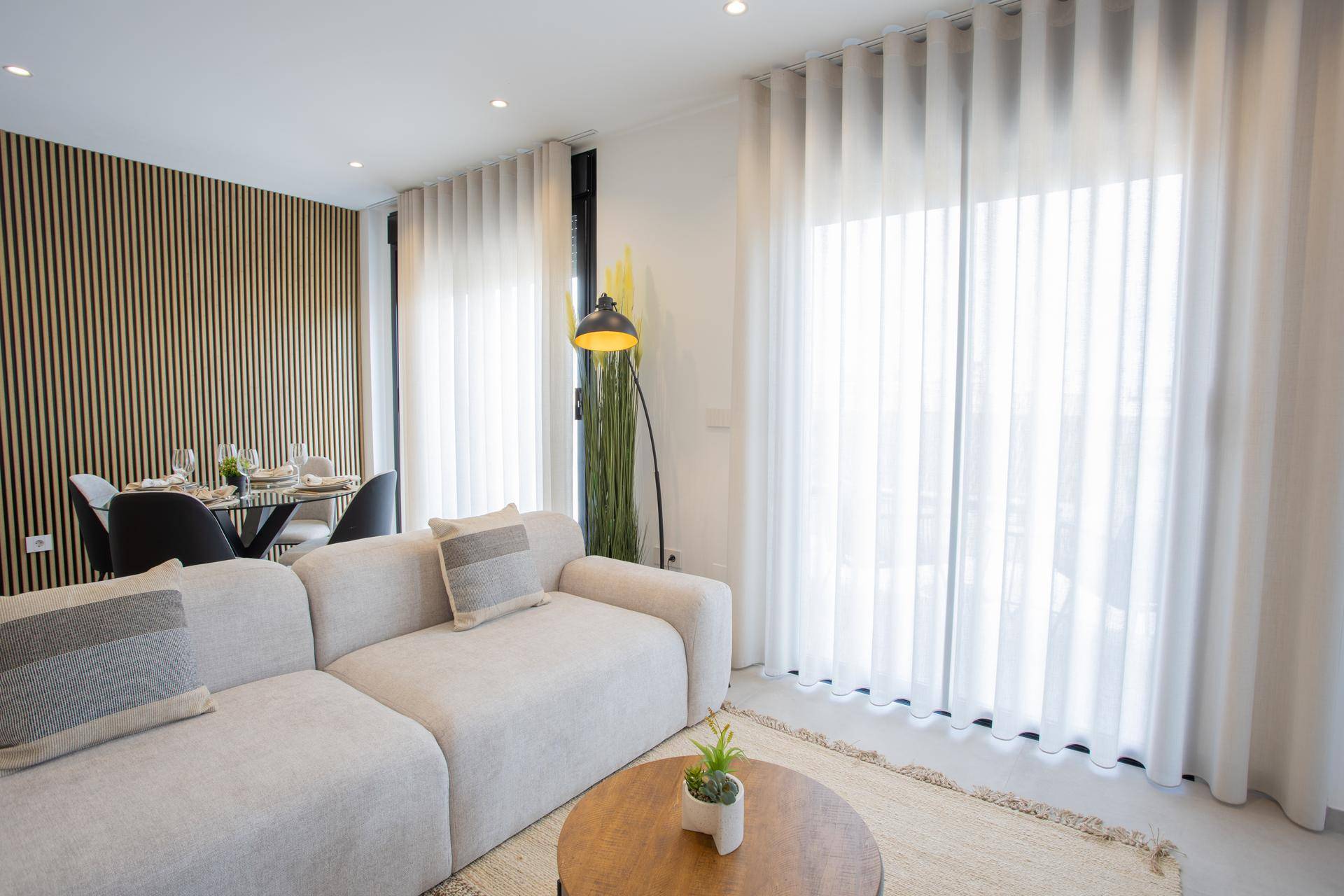 Helles Wohnzimmer mit großem Sofa, Stehlampe und bodentiefen Fenstern mit Vorhängen.