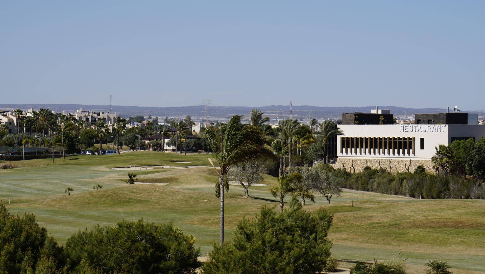 Grüner Golfplatz mit einem Restaurantgebäude im Hintergrund und weitem Blick.