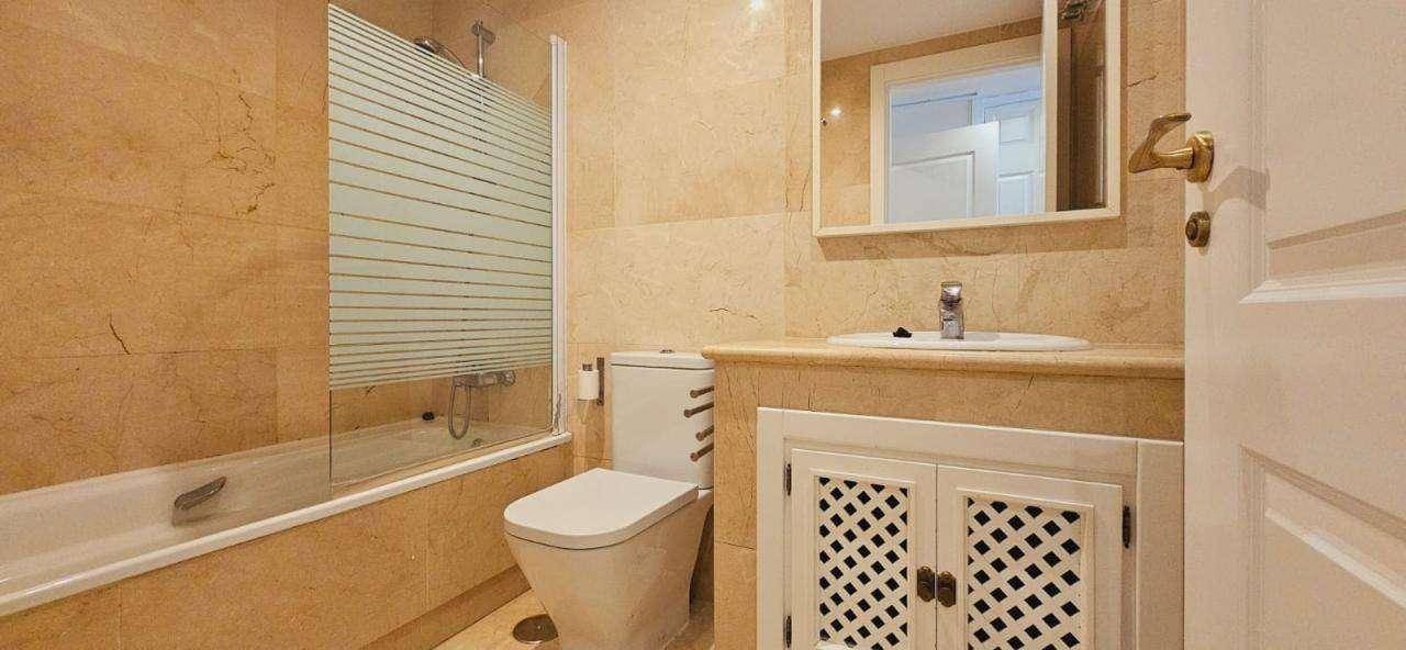 Modernes Badezimmer mit beigefarbenen Fliesen, Badewanne mit Duschwand und Waschtisch.