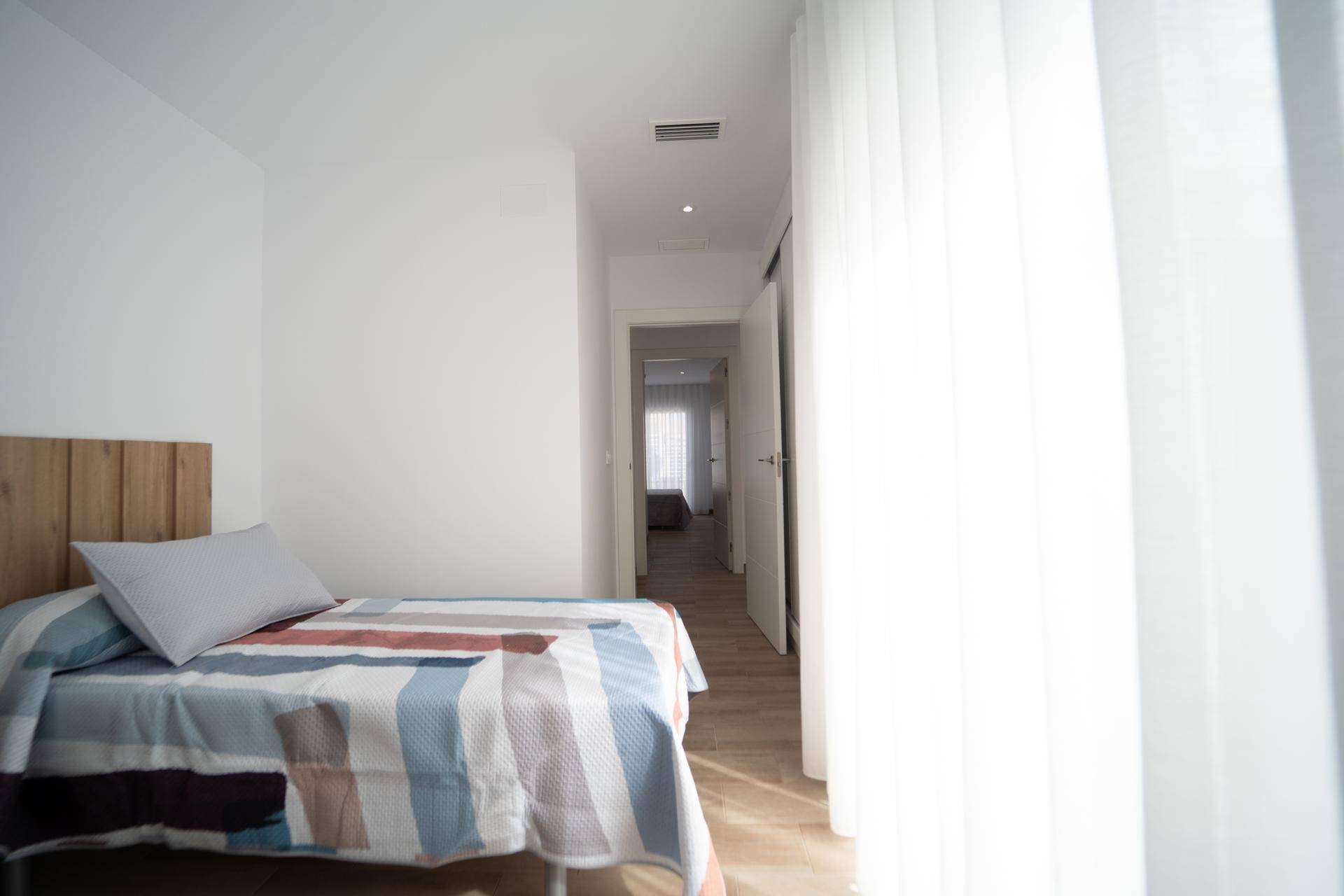 Schlafzimmer mit Einzelbett, Holz-Kopfteil und großem Fenster mit hellen Vorhängen.