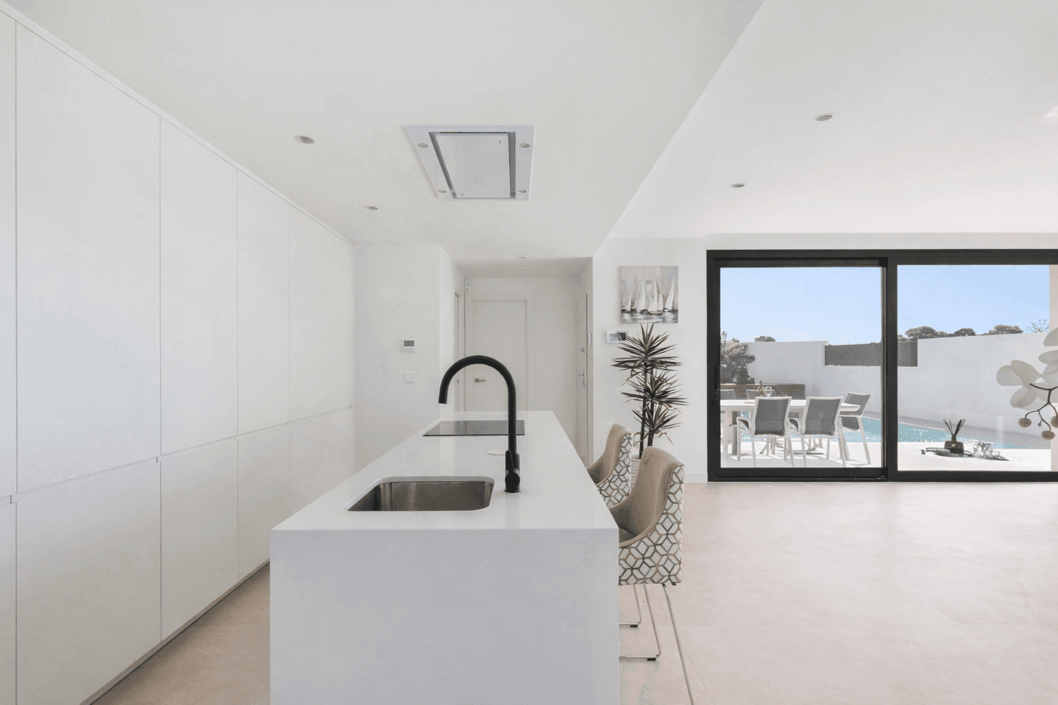 Moderne weiße Küche mit Kochinsel und direktem Zugang zur Terrasse.