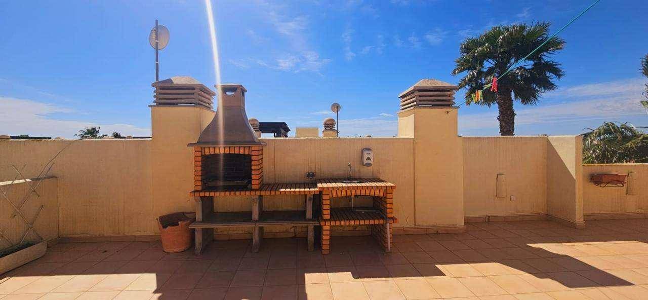 Große Dachterrasse mit gemauertem Grillbereich und weitem Blick unter blauem Himmel.