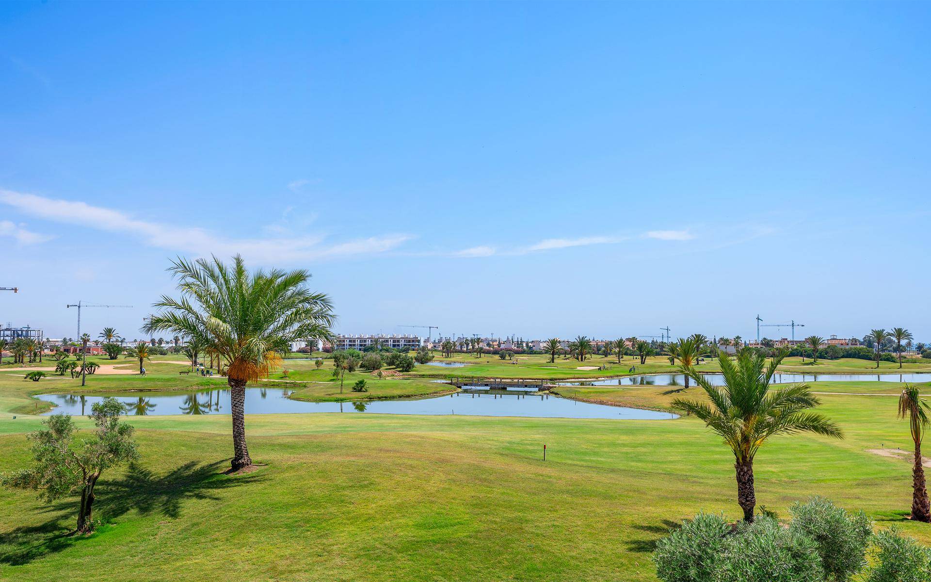 Weitläufiger Golfplatz mit Wasserhindernissen und Palmen unter strahlend blauem Himmel.