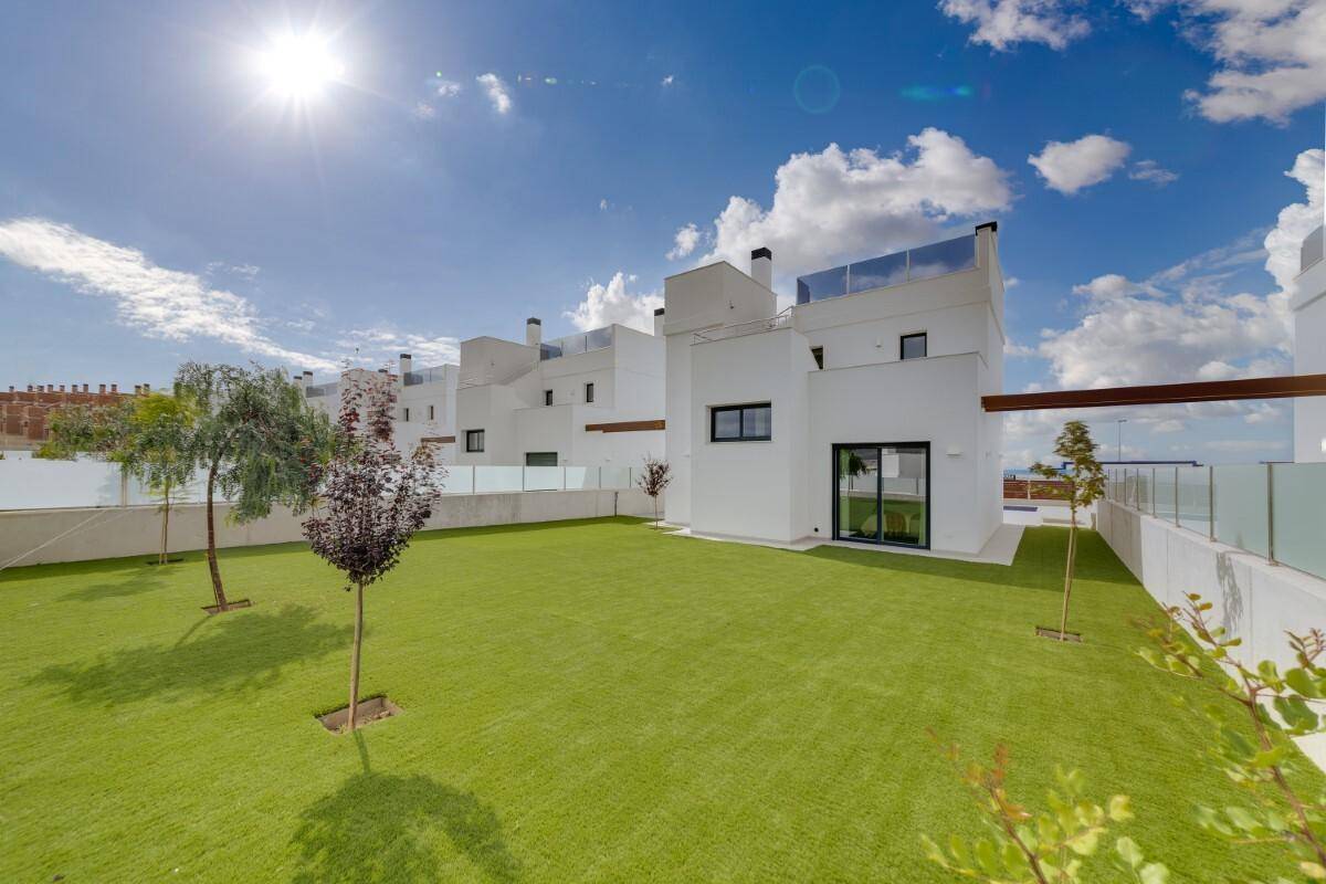 Sonniger Gartenbereich mit Kunstrasen und jungen Bäumen neben der modernen Villa.