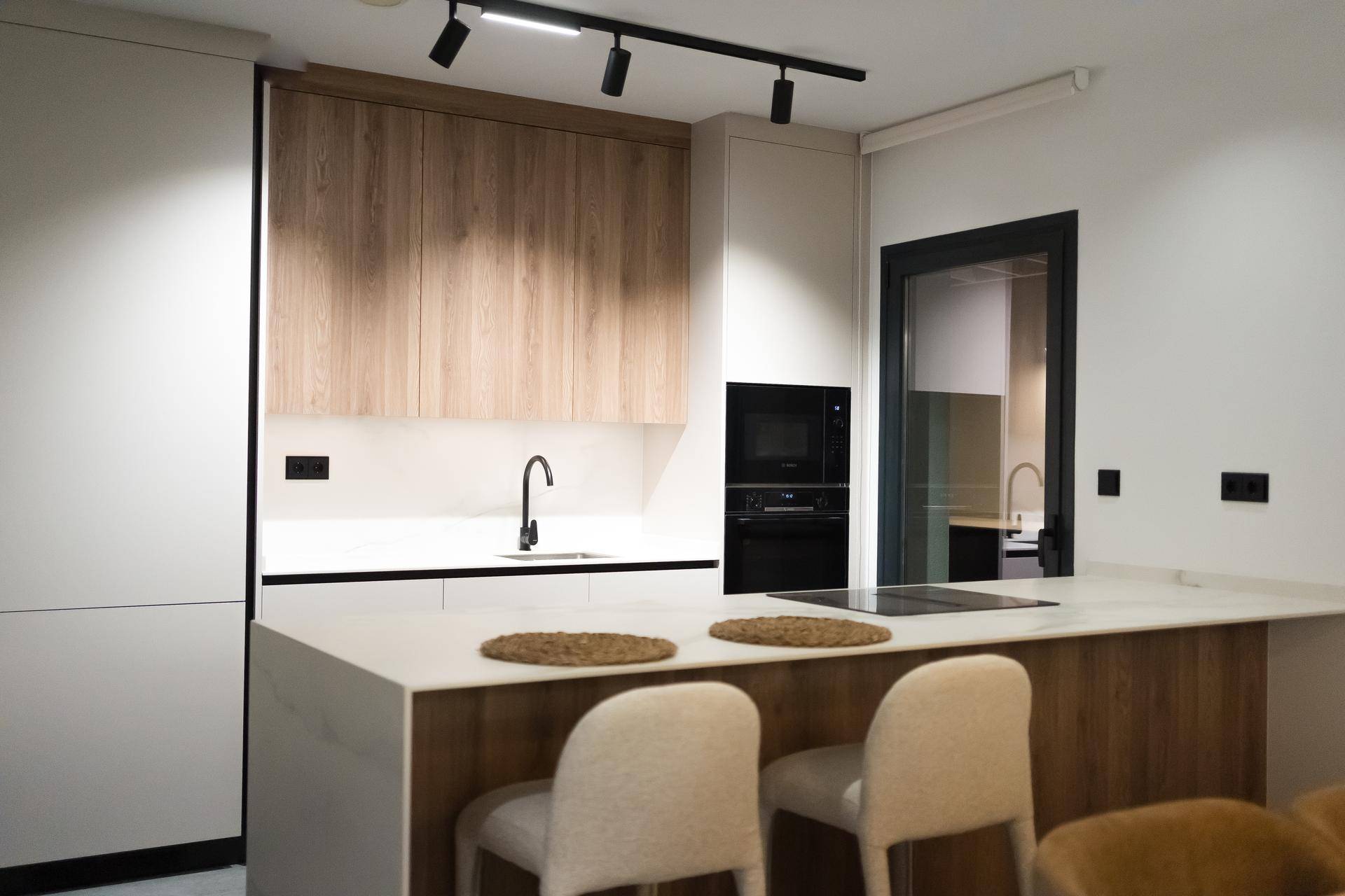 Moderne Einbauküche mit Holz- und Weißfronten, Kücheninsel und integrierten Geräten.