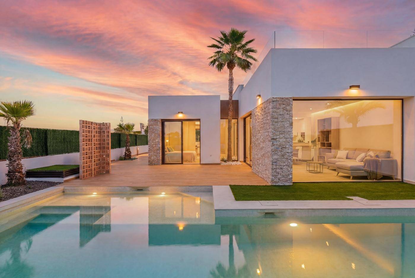 Luxuriöse Villa mit großem Poolbereich und Holzterrasse unter einem farbenprächtigen Abendhimmel.