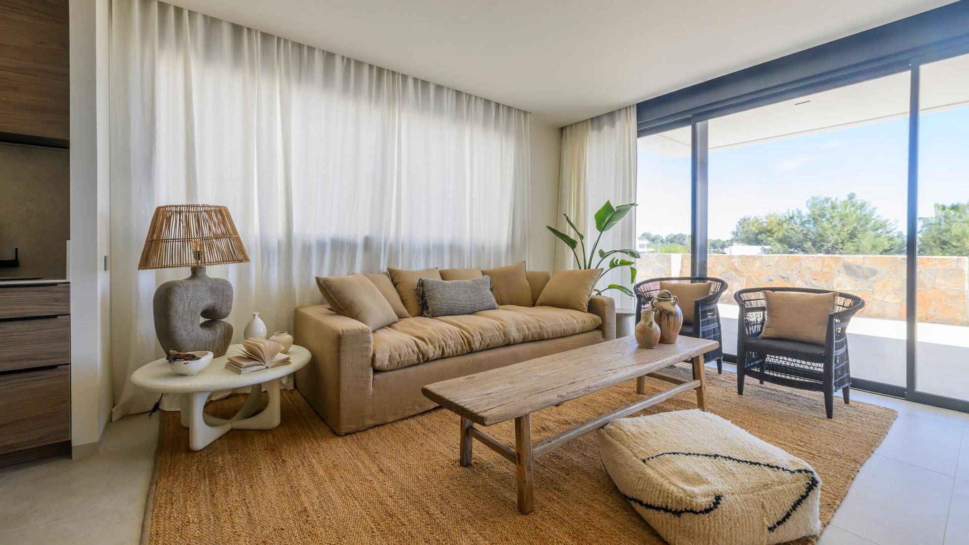 Heller Wohnbereich mit beigem Sofa, Holztisch und zwei schwarzen Korbstühlen, umgeben von transparenten Vorhängen.