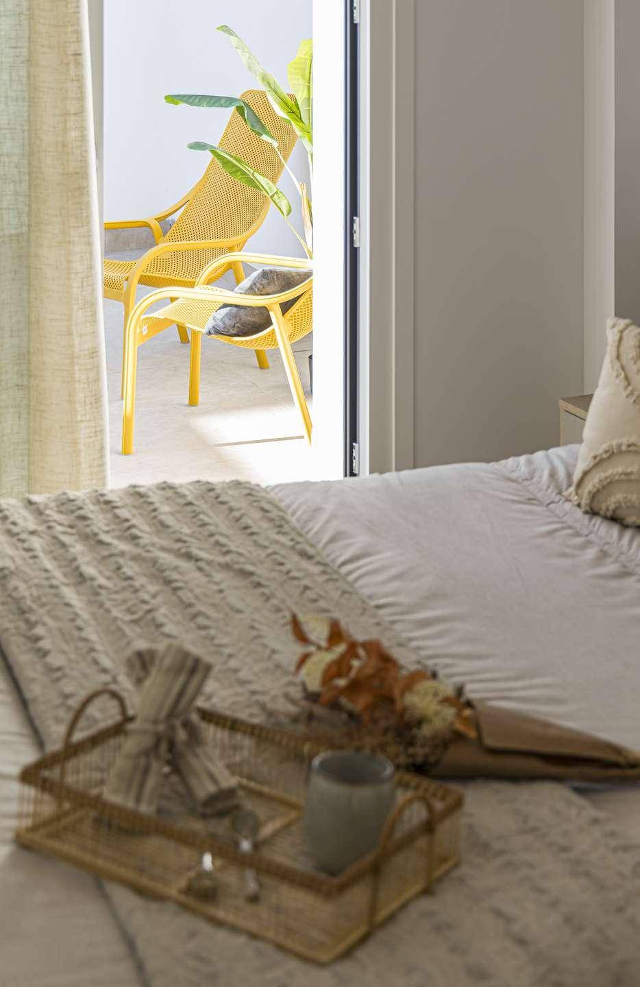 Schlafzimmer mit direktem Zugang zu einer sonnigen Terrasse, ausgestattet mit gelben Stühlen.