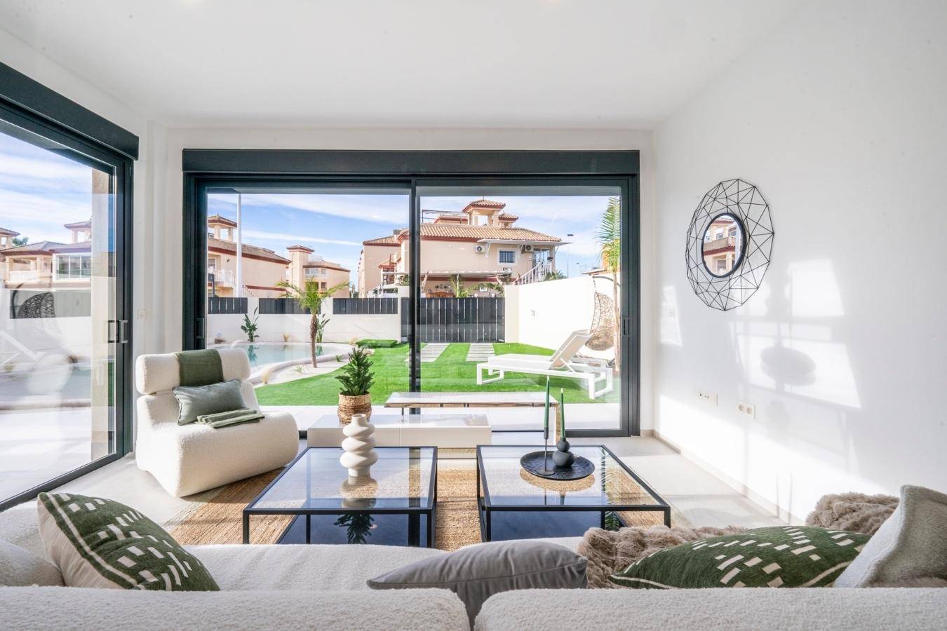 Helles Wohnzimmer mit modernem Sofa und direktem Blick auf den gepflegten Garten und den Swimmingpool.