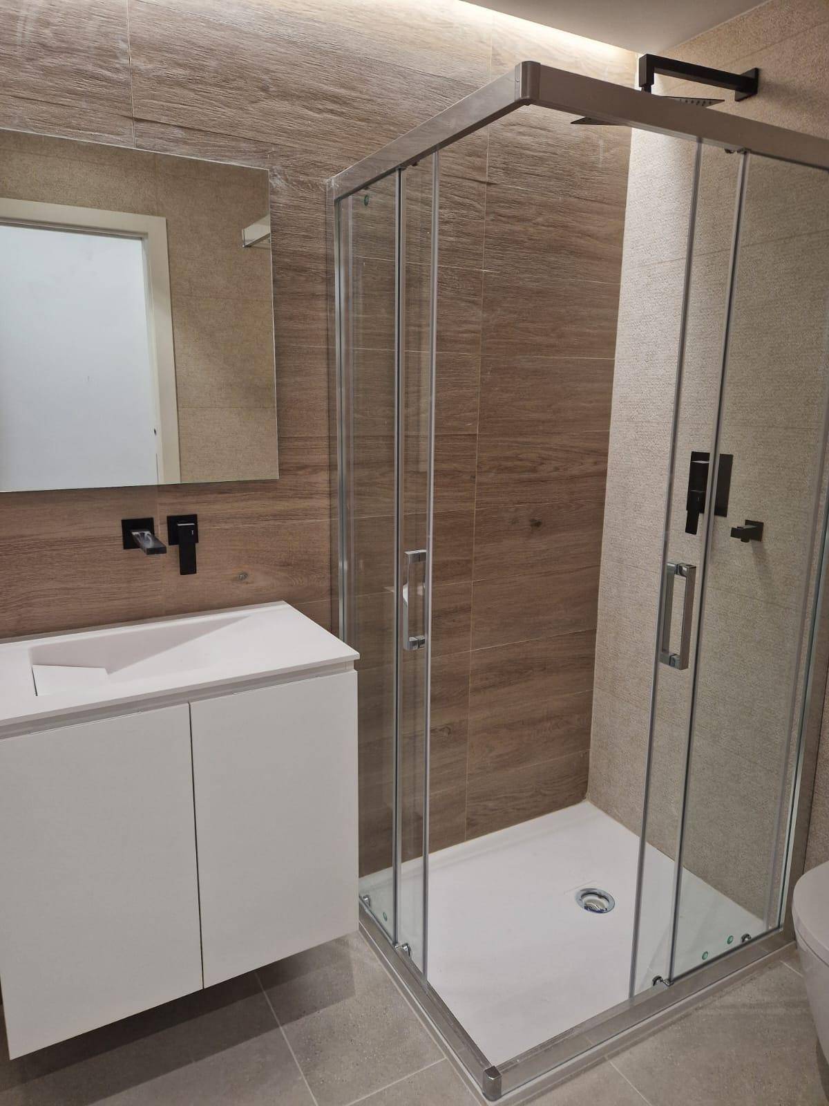 Modernes Badezimmer mit Duschkabine, Einzelwaschbecken und Fliesen in Holzoptik.