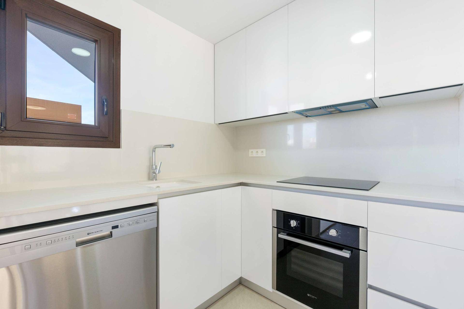 Helle Küche mit Fenster, Spülmaschine, Induktionskochfeld und weißen Oberschränken.