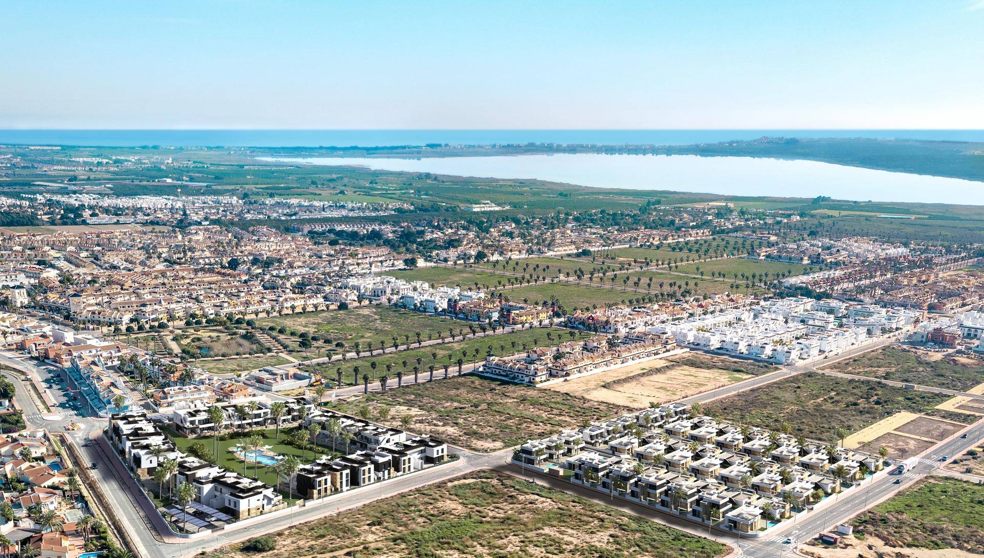 Luftaufnahme einer Wohnsiedlung mit Neubauten, umgeben von Natur, See und Meerblick.