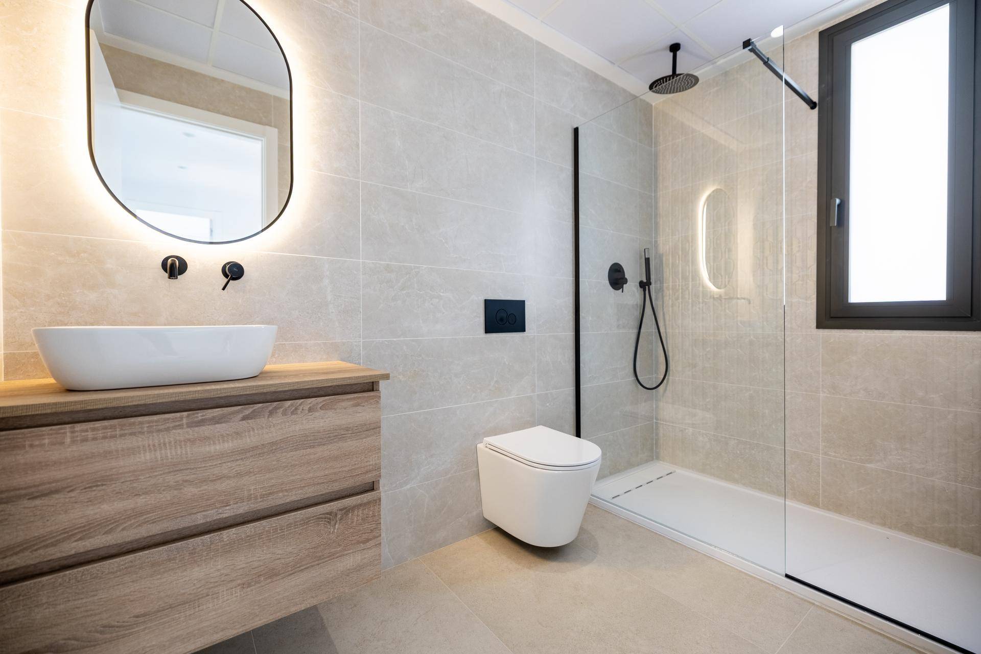Elegantes Badezimmer mit großformatigen Fliesen, beleuchtetem Spiegel und bodengleicher Dusche.