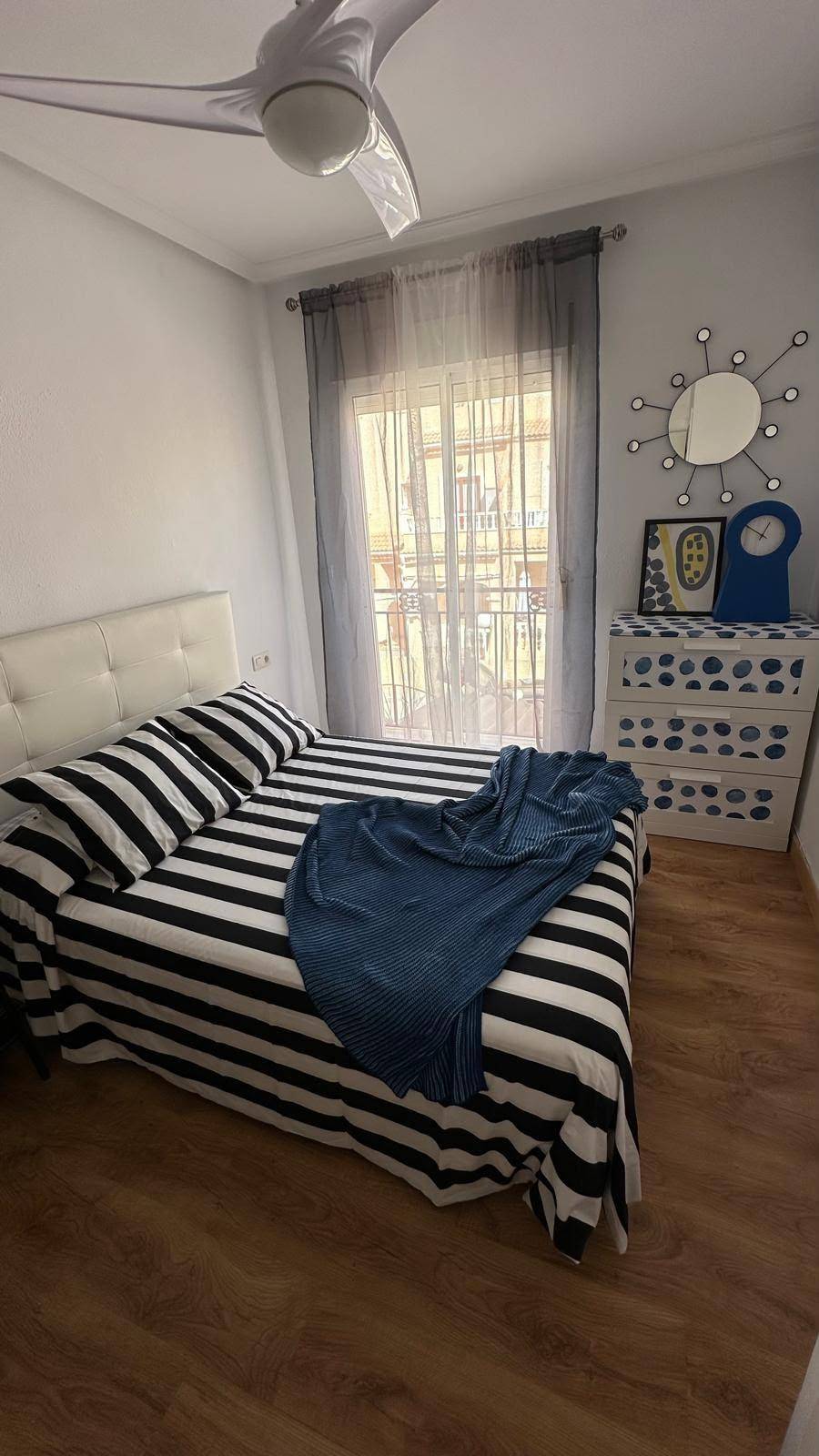 Schlafzimmer mit gestreifter Bettwäsche, Holzboden und einem Nachttisch mit Dekoration.