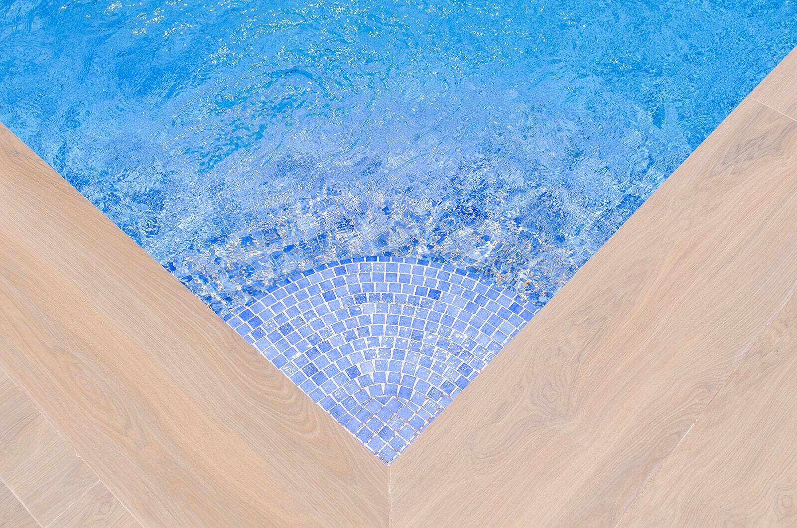 Detailaufnahme einer Poolecke mit blauen Mosaikfliesen und Holzoptik-Boden.