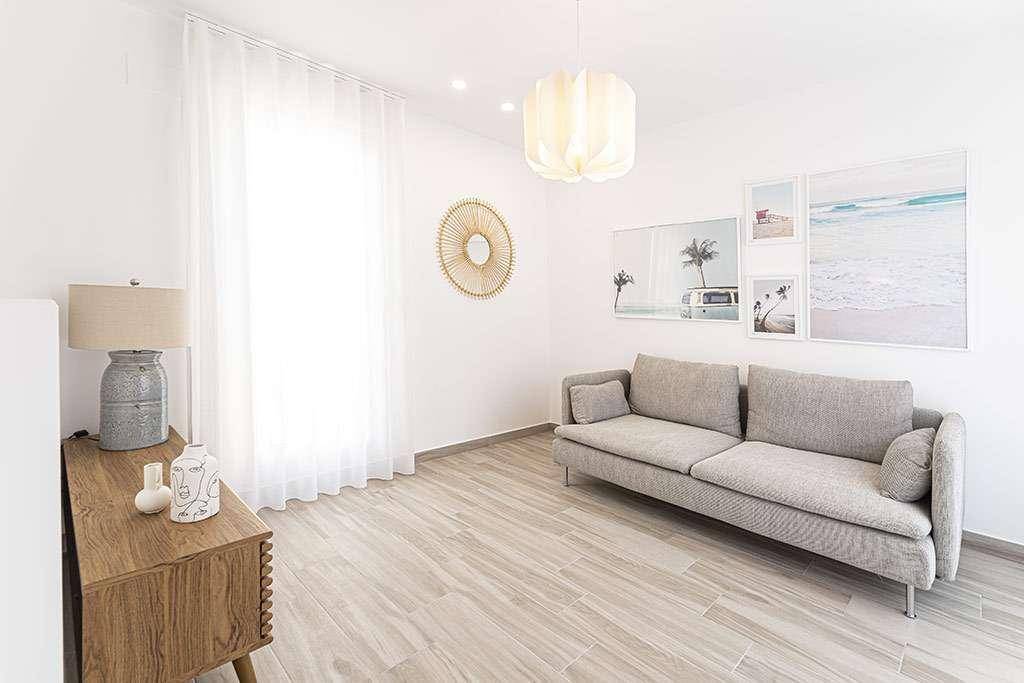 Gemütliches Wohnzimmer mit hellem Sofa, Holztisch und maritimen Bildern an der Wand.