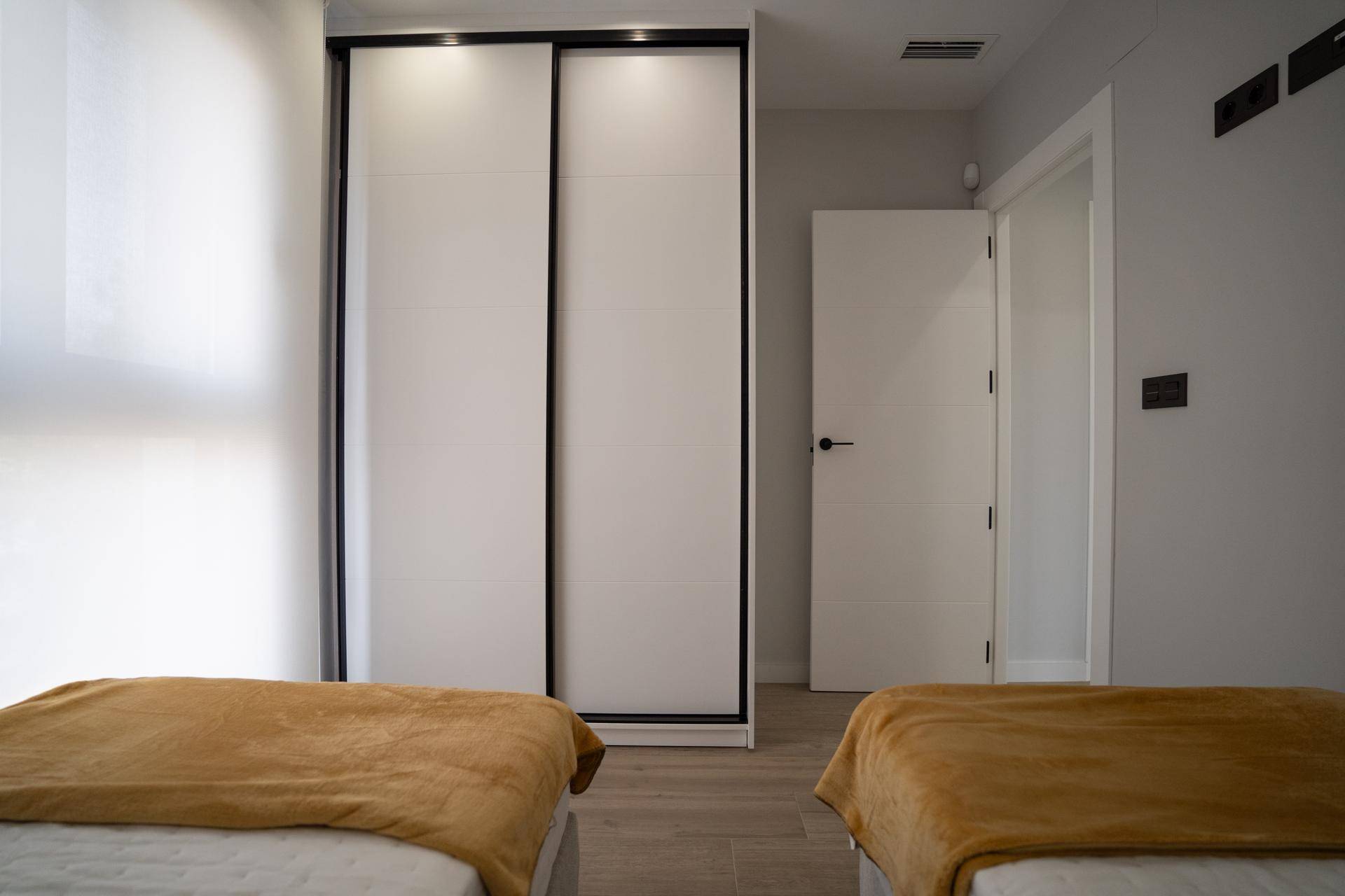 Schlafzimmer mit zwei Einzelbetten, Einbauschrank und hellem Holzboden.