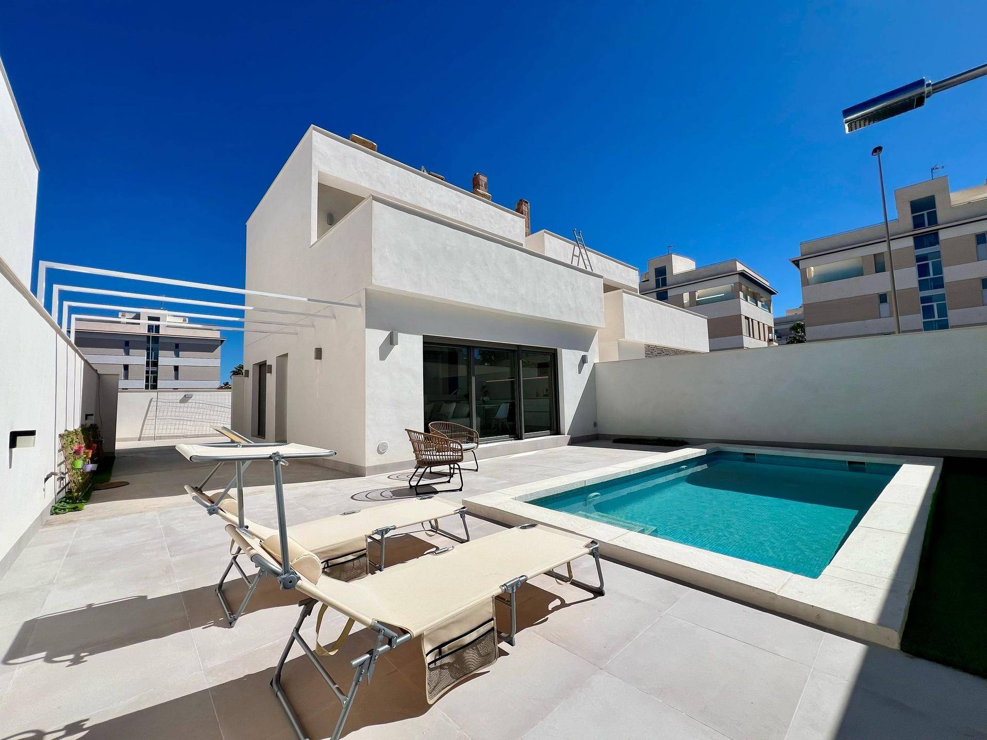 Sonnige Terrasse mit privatem Pool und Liegestühlen vor der modernen Hausfassade.