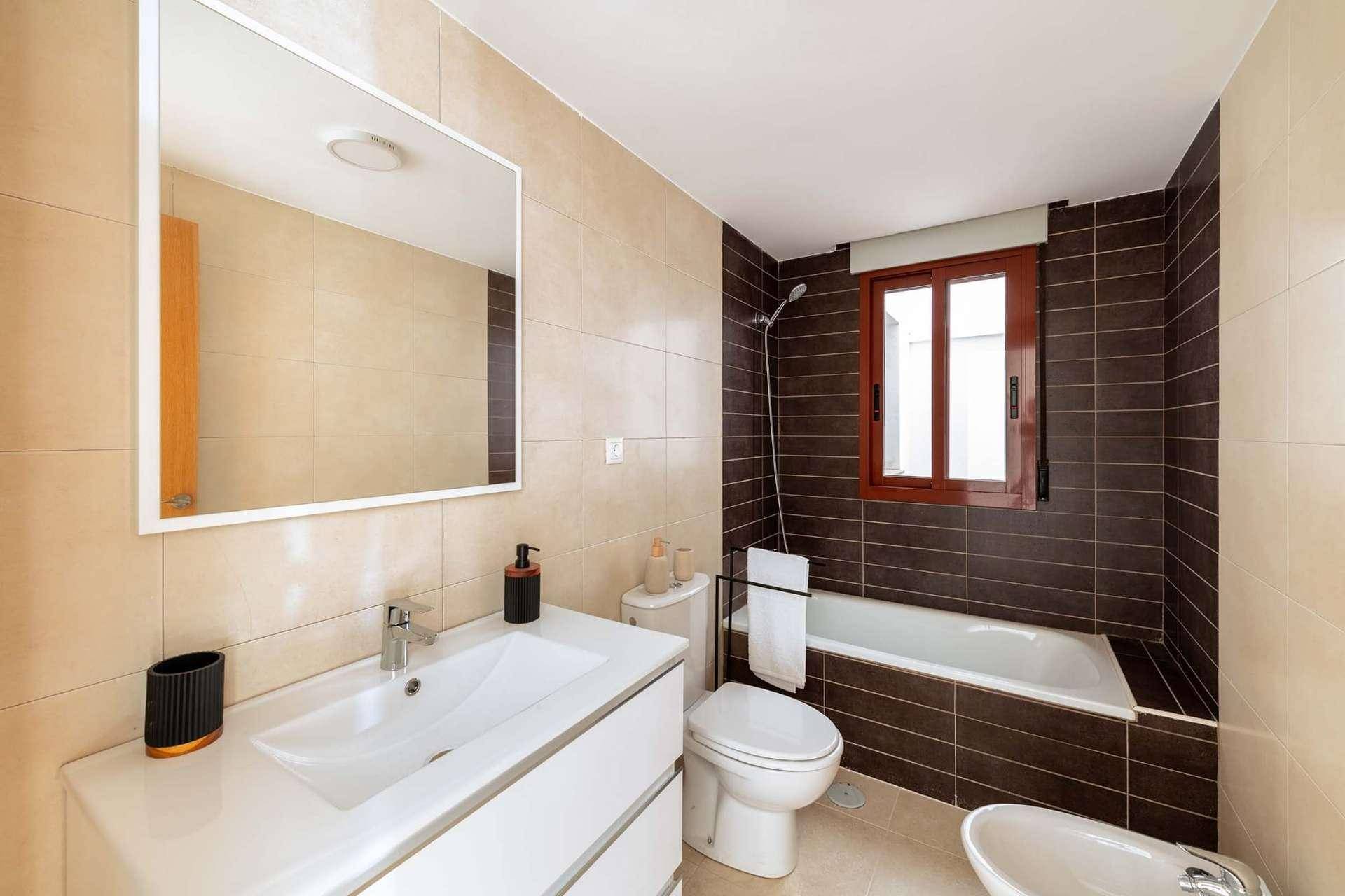 Modernes Badezimmer mit Badewanne, Waschtisch und Bidet, ausgestattet mit braunen und beigen Fliesen.