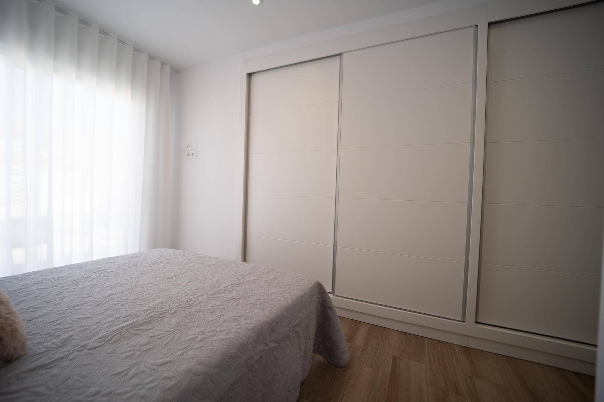 Helles Schlafzimmer mit großem Bett und geräumigen weißen Schiebetürenschränken.