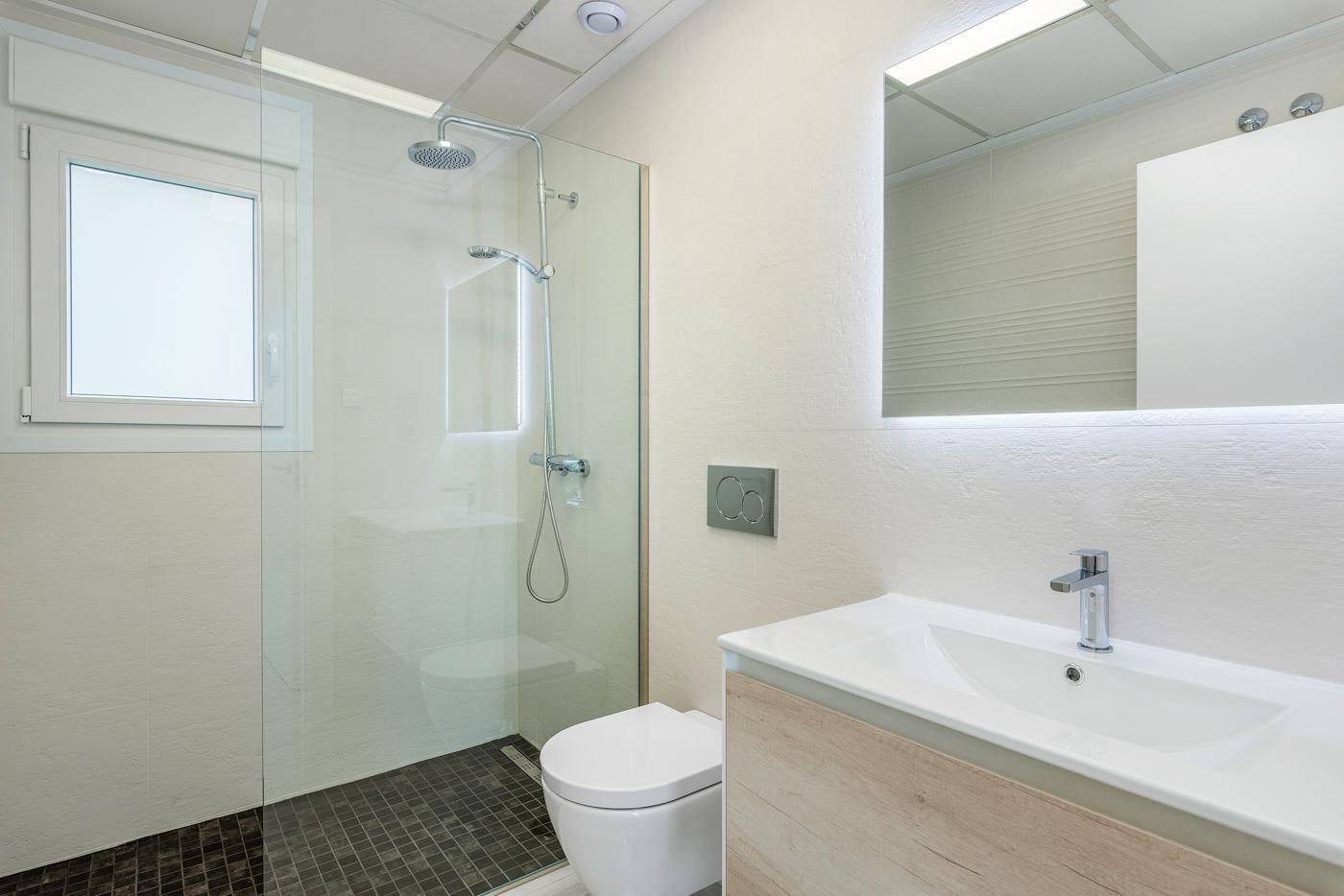 Modernes Badezimmer mit begehbarer Dusche, wandhängendem WC und Fenster für natürliches Licht.