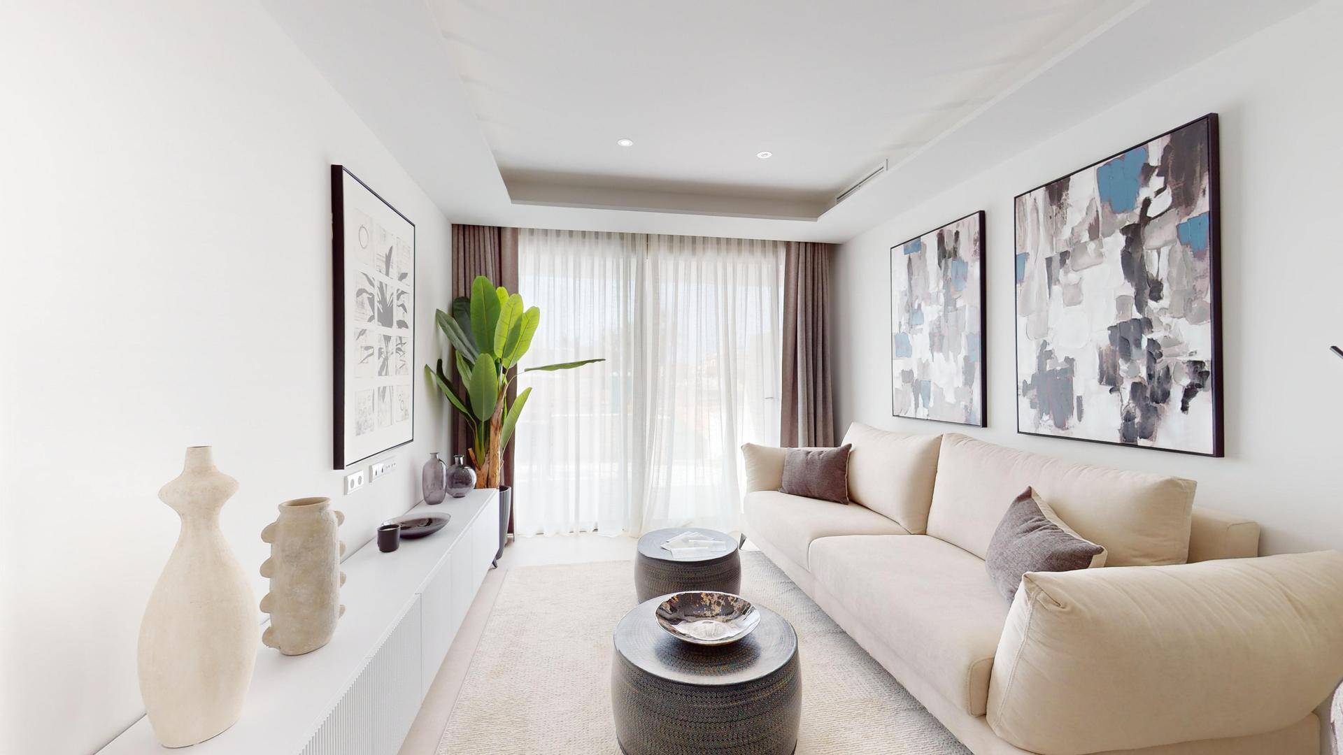 Gemütliches Wohnzimmer mit hellem Sofa, modernen Kunstwerken und großen Fenstern.