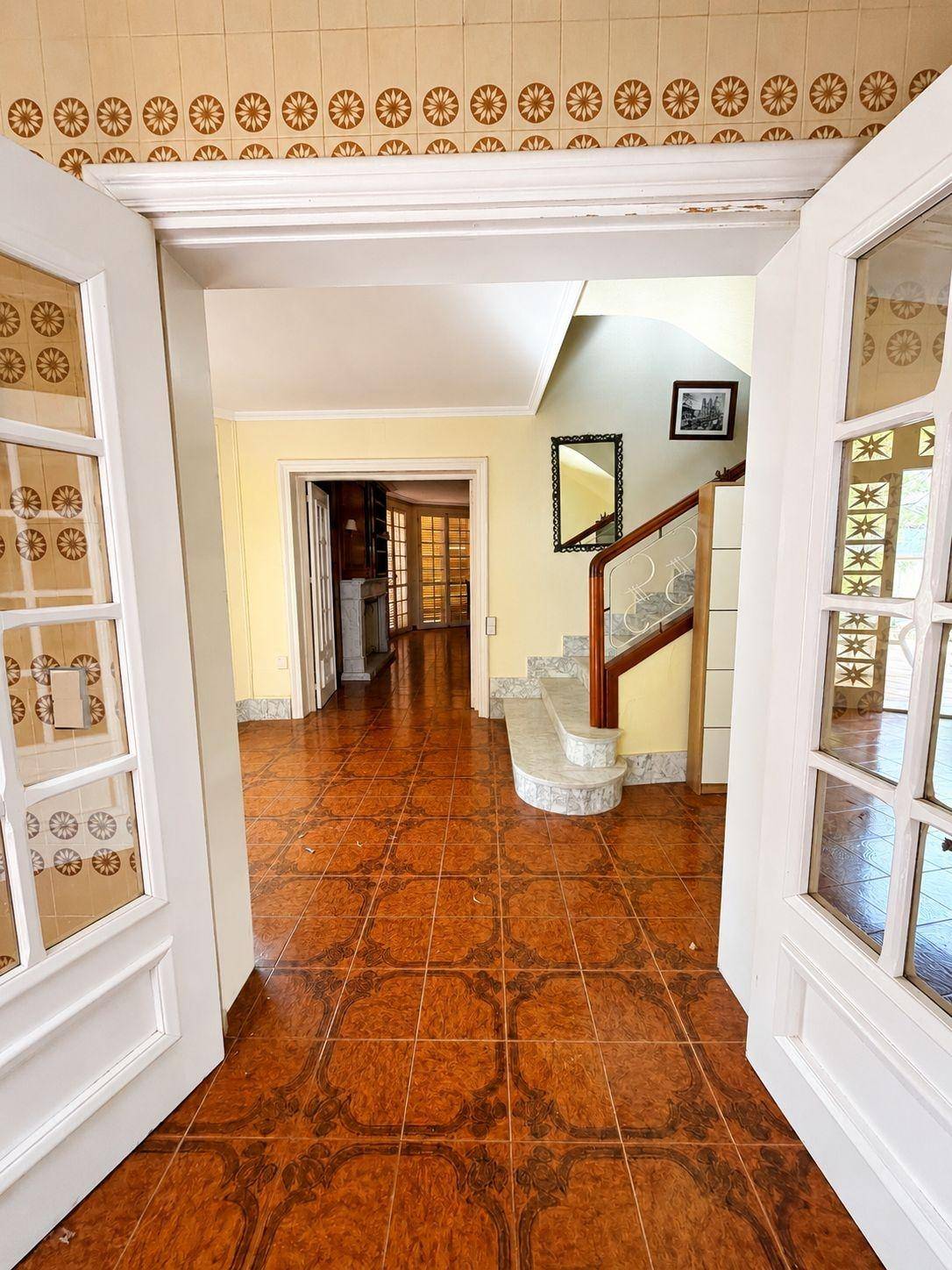 Geräumiger Eingangsbereich mit gemusterten Terrakottafliesen, gelben Wänden und einer eleganten Treppe.