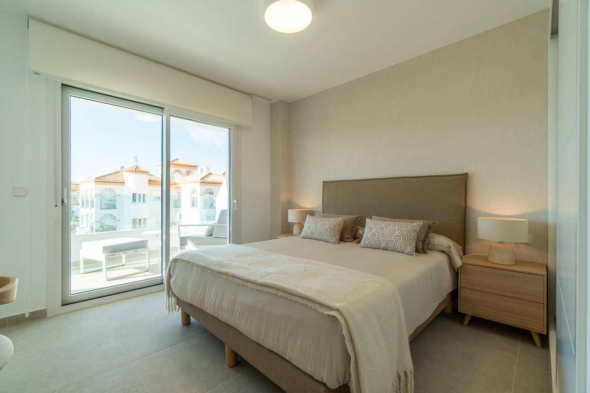 Helles Schlafzimmer mit Doppelbett und großen Schiebetüren, die zu einem Balkon führen.