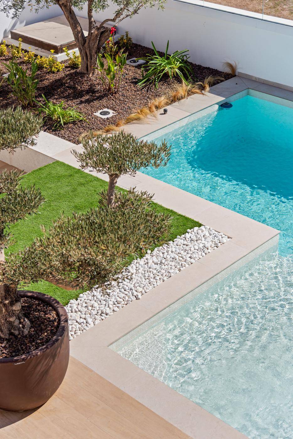 Detailansicht des Pools mit angrenzendem Rasen und dekorativen weißen Steinen im Garten.