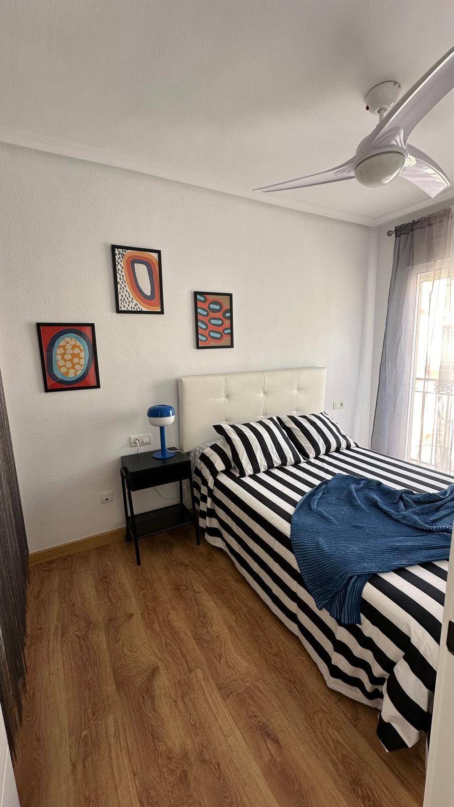 Schlafzimmer mit gestreifter Bettwäsche, Holzboden und farbenfrohen Bildern an der Wand.