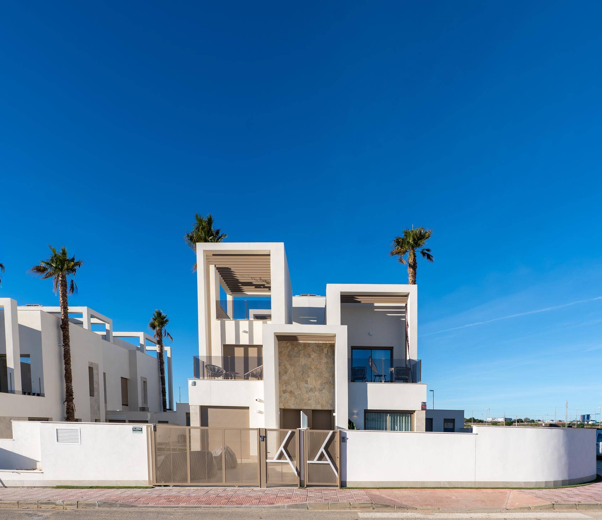 Moderne weiße Villa mit klaren Linien, Balkonen und Palmen unter strahlend blauem Himmel.