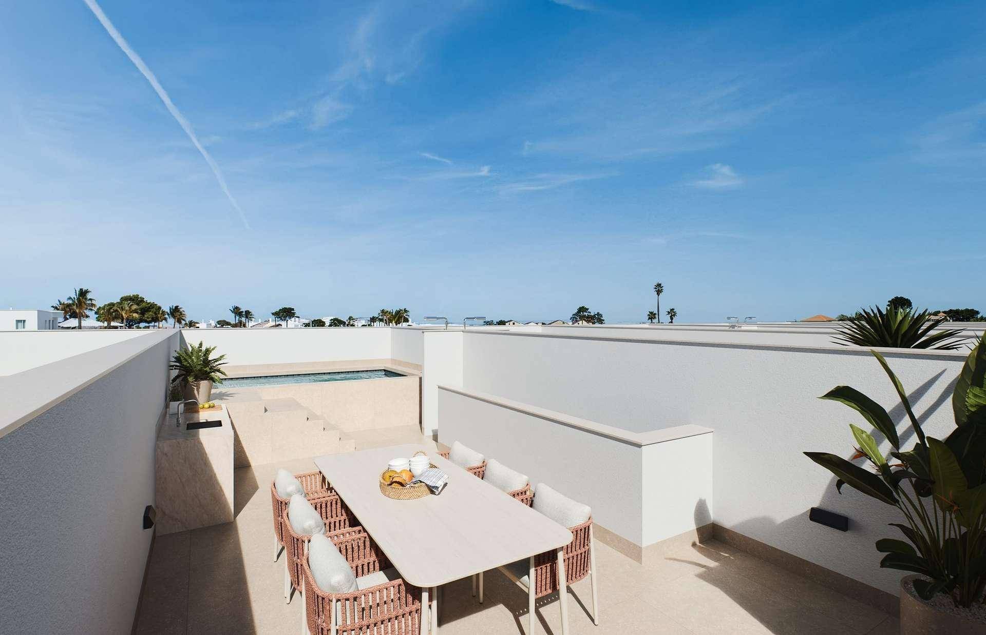 Große Dachterrasse mit modernem Esstisch und Stühlen, umgeben von weißen Mauern und Pflanzen.