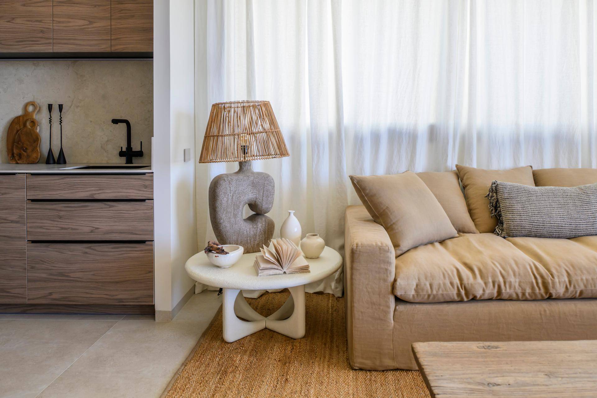Heller Wohnbereich mit beigem Sofa, Beistelltisch und dekorativer Lampe, ergänzt durch transparente Vorhänge.