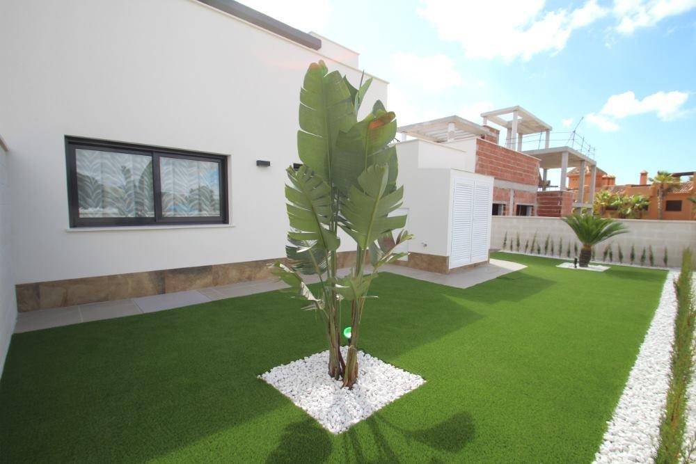 Gepflegter Gartenbereich mit Kunstrasen, Palmen und weißen Ziersteinen.