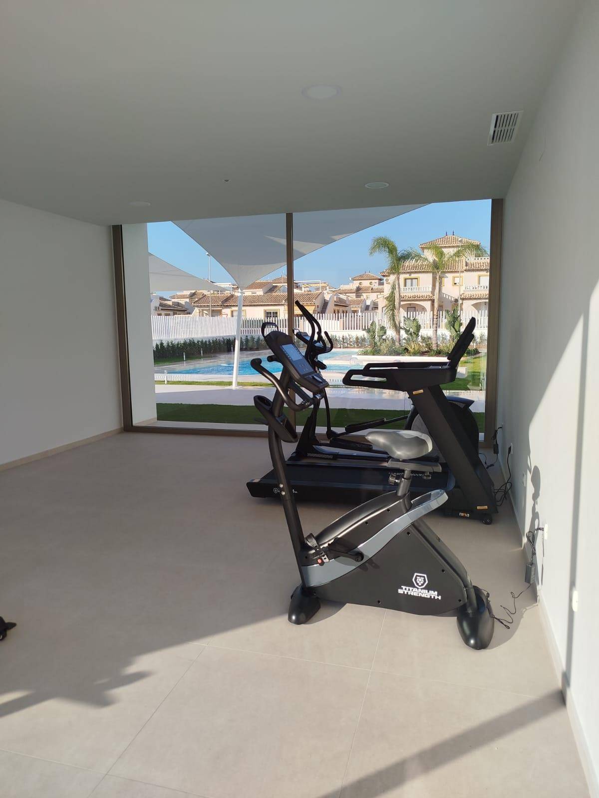 Fitnessraum mit Trainingsgeräten und großen Fenstern mit Blick auf den Pool und die Wohnanlage.