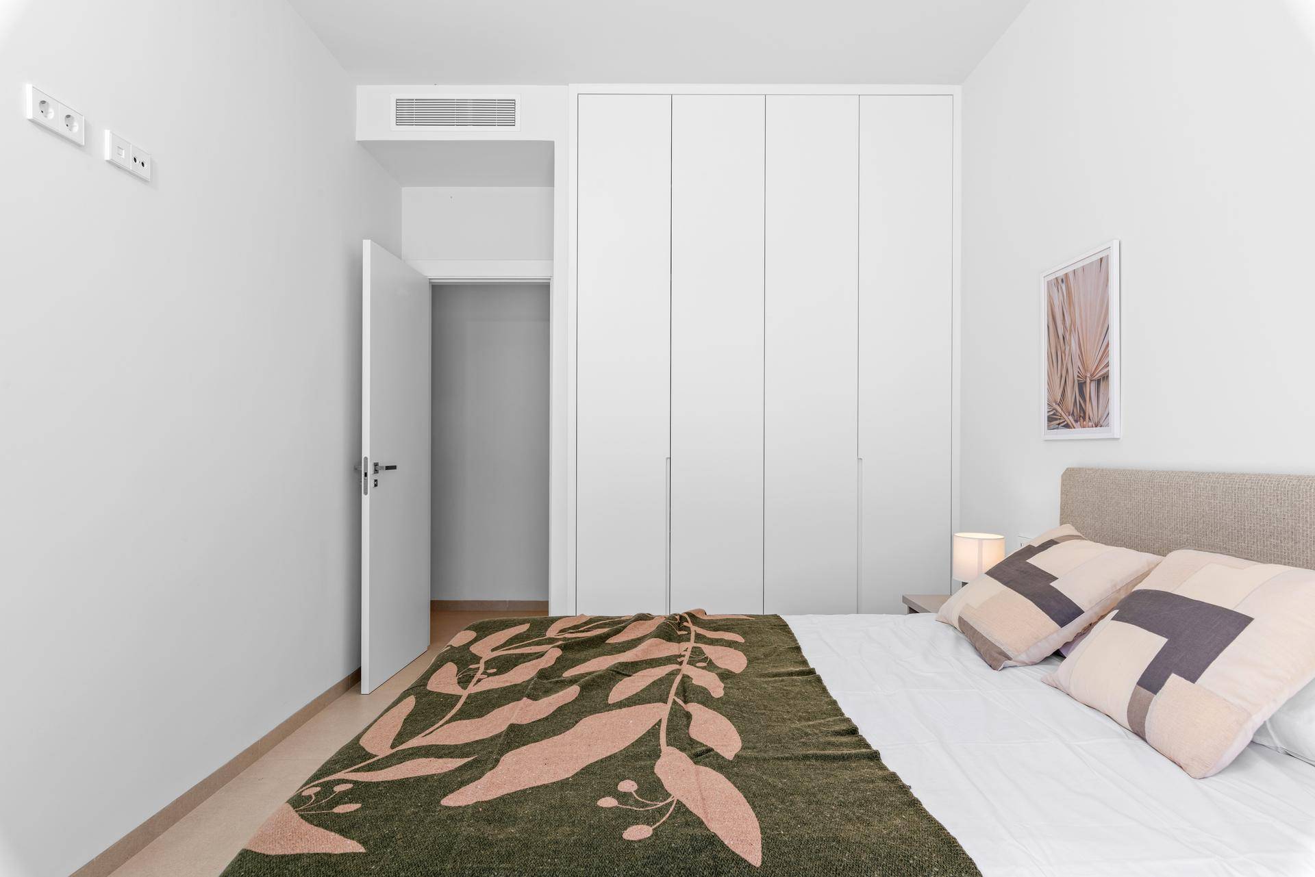 Helles Schlafzimmer mit Einbauschränken, modernem Bett und Zugang zu einem weiteren Raum.